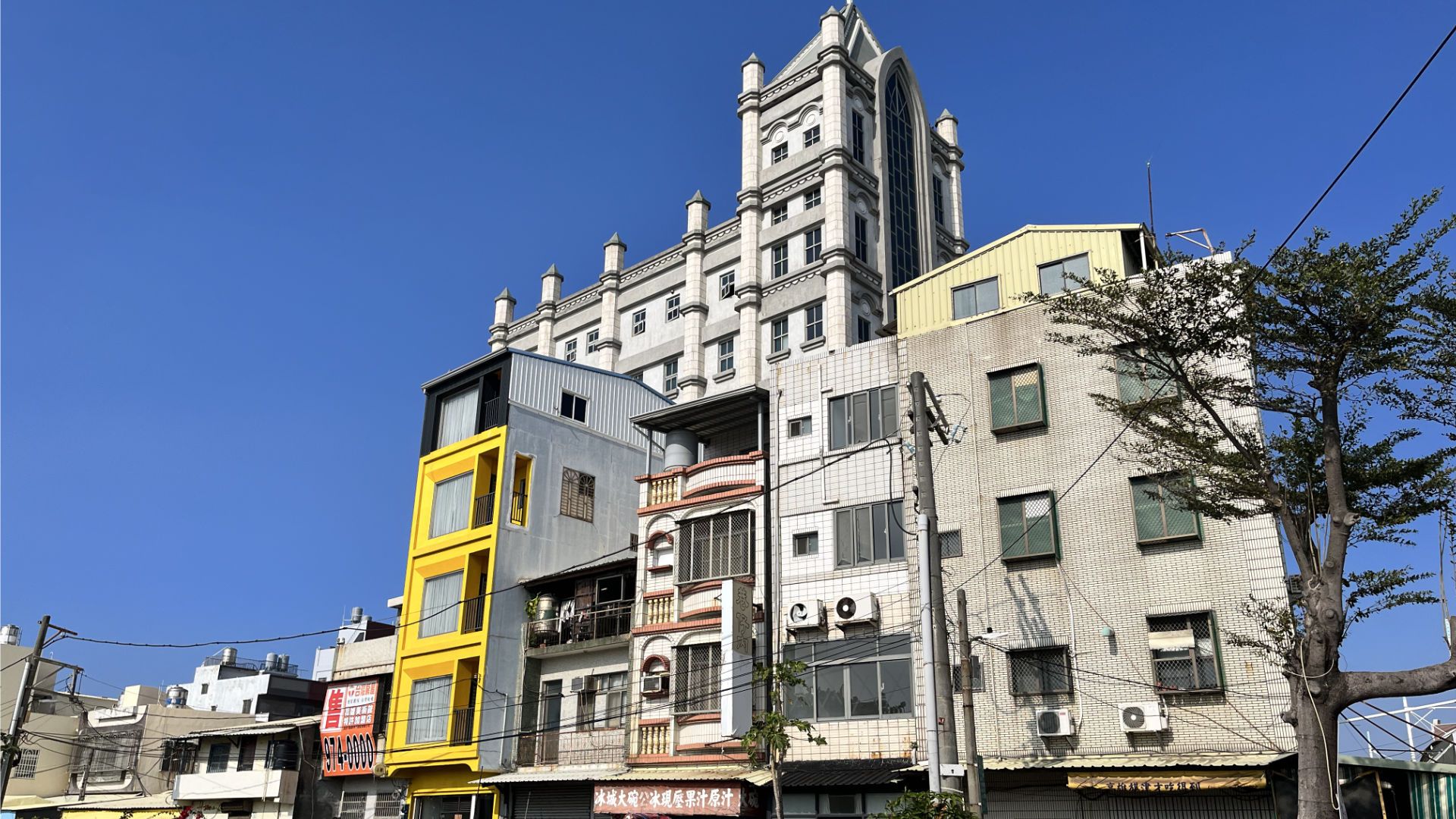 A tall church rising up behind some four-level buildings.