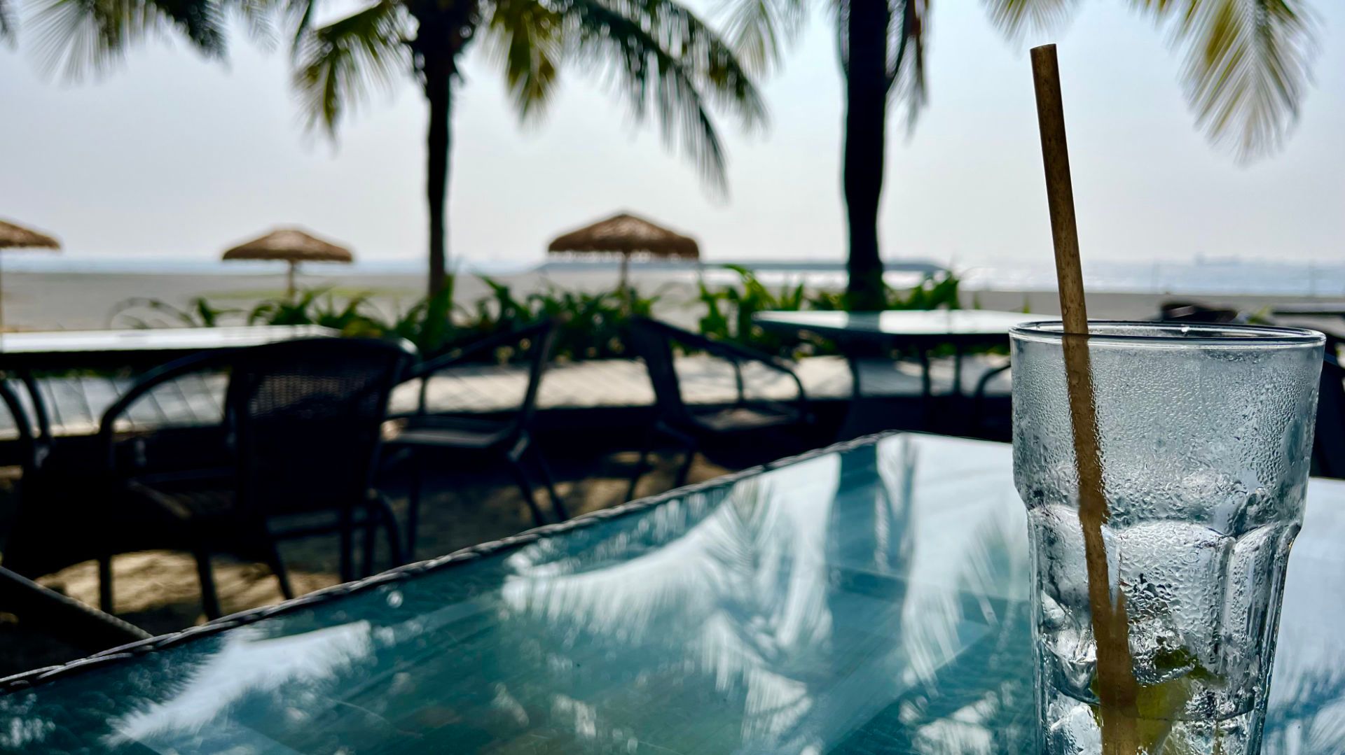 A glass of gin and tonic on a table at a beachside bar.