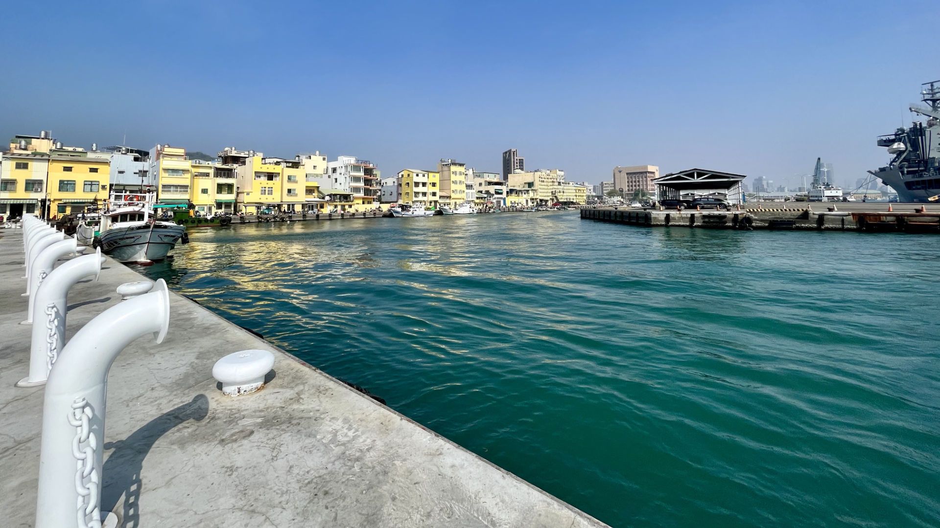 A row of pastel-coloured three- and four-level houses overlooking the harbor, with a naval vessel on the right.