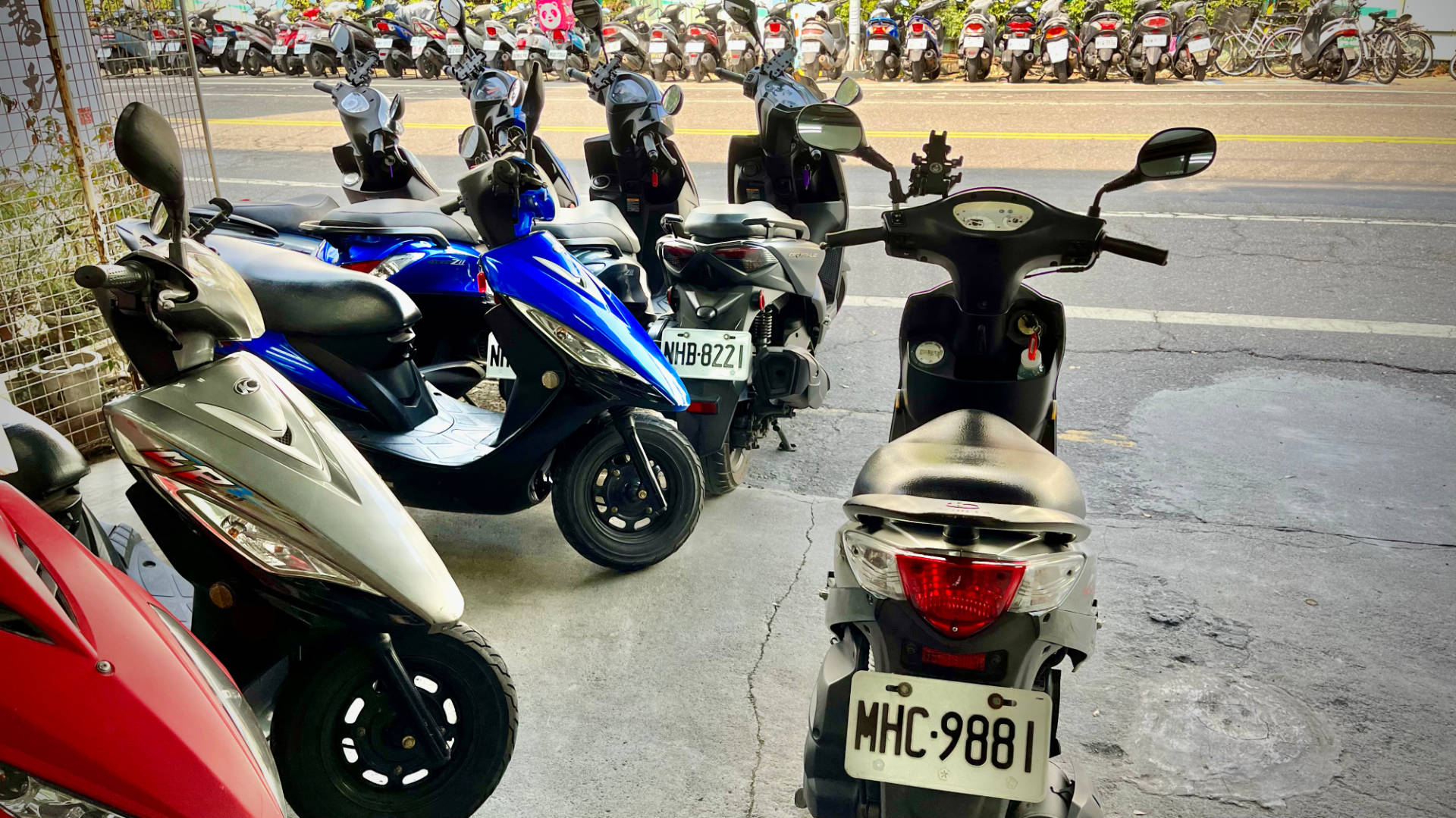 A motorbike with the license plate MHC9881 in the foreground, with dozens of other scooters parked either side of the road.