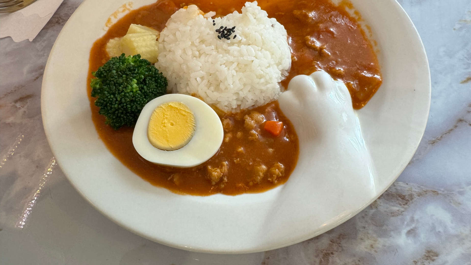 A bowl of curry, vegetables, egg, and rice. The bowl has a cat-paw-like shape raised on the front of it.