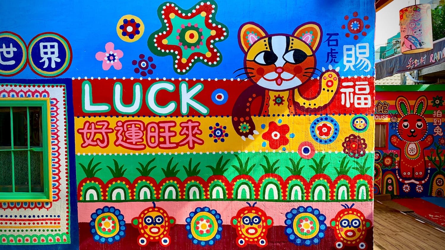 A Taiwan Leopard Cat mascot painted on the wall of a house in Rainbow Village. Next to the cat, the word LUCK is painted on the wall.