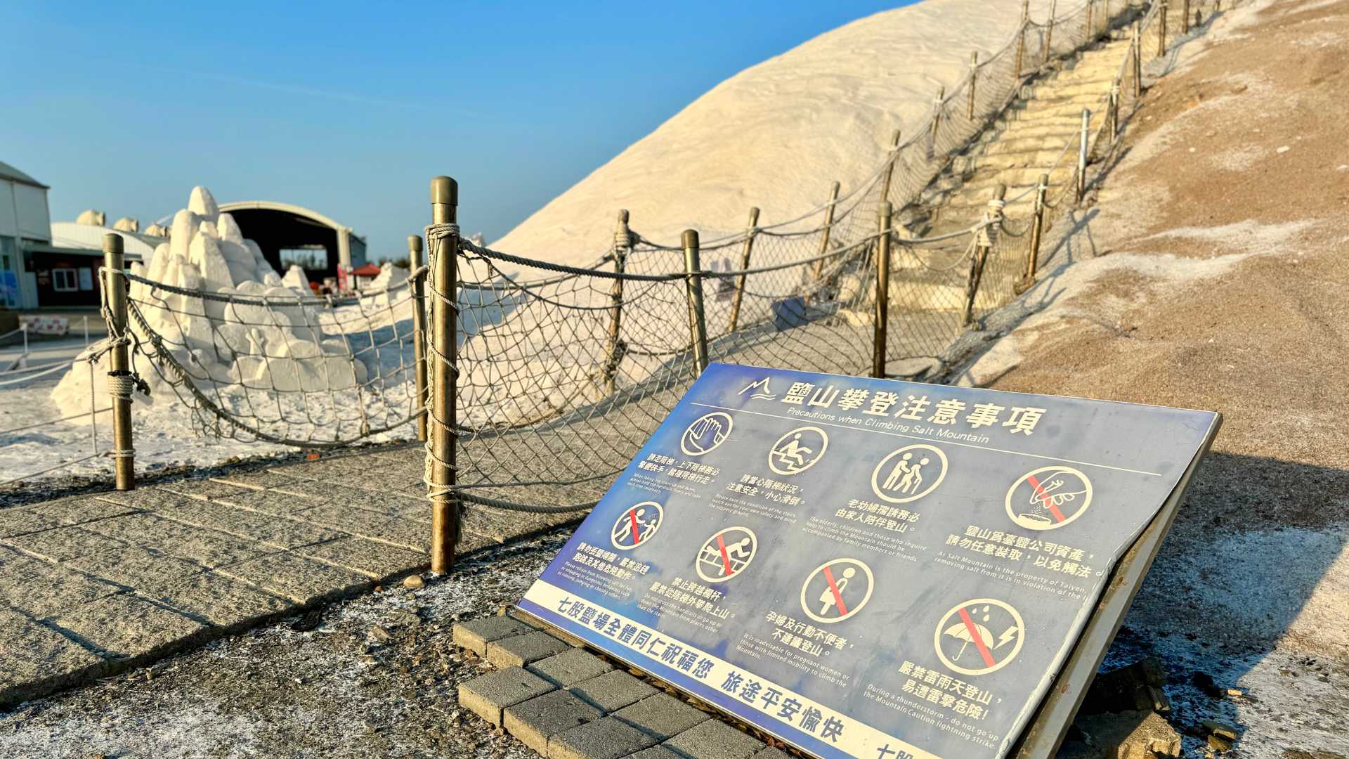 A sign labeled ‘Precautions when Climbing Salt Mountain’, with eight rules listed. Steps caved into the mountain are visible behind.