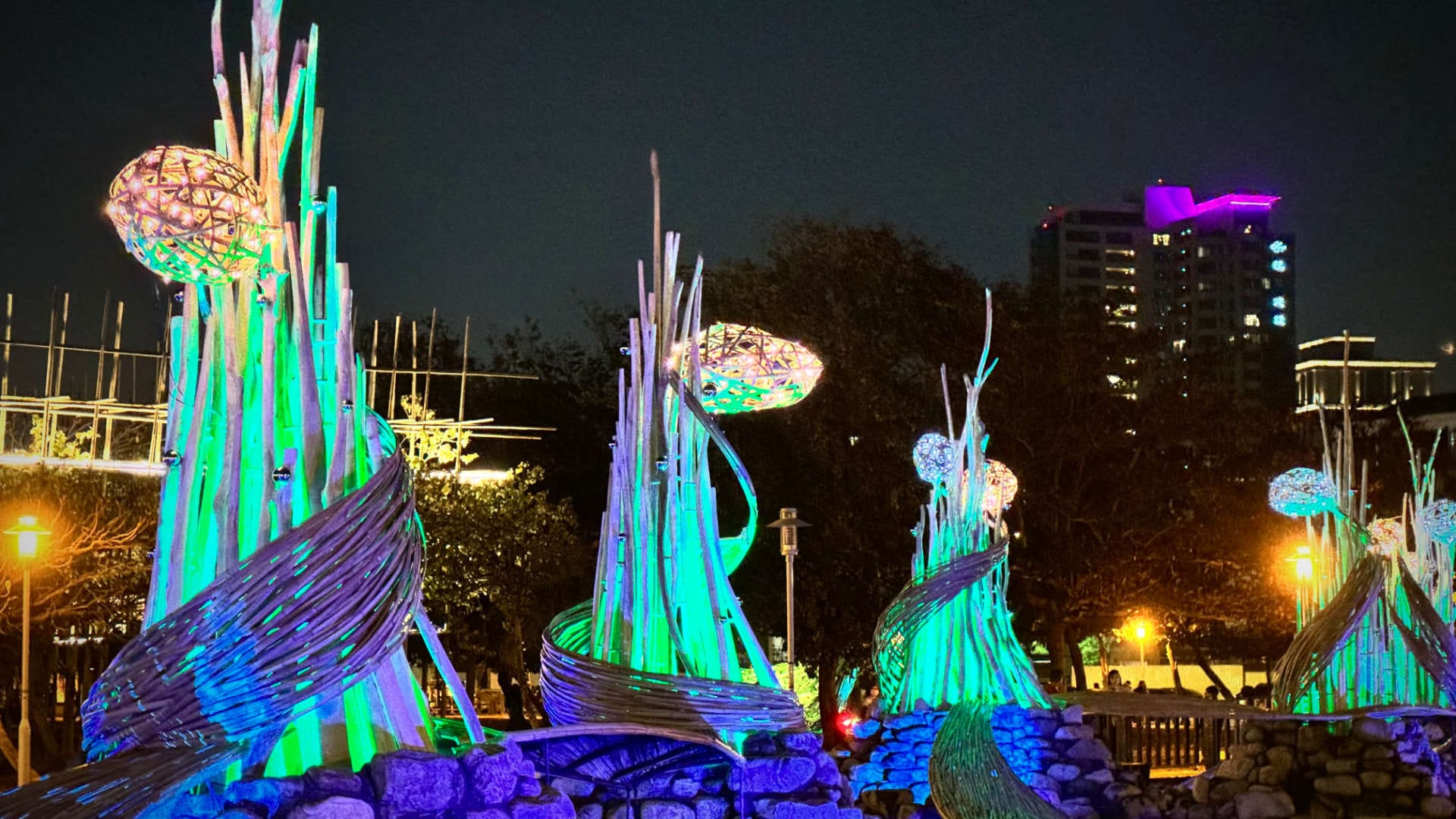 A series of illuminated tall abstract sculptures that have plant-like buds near the top.