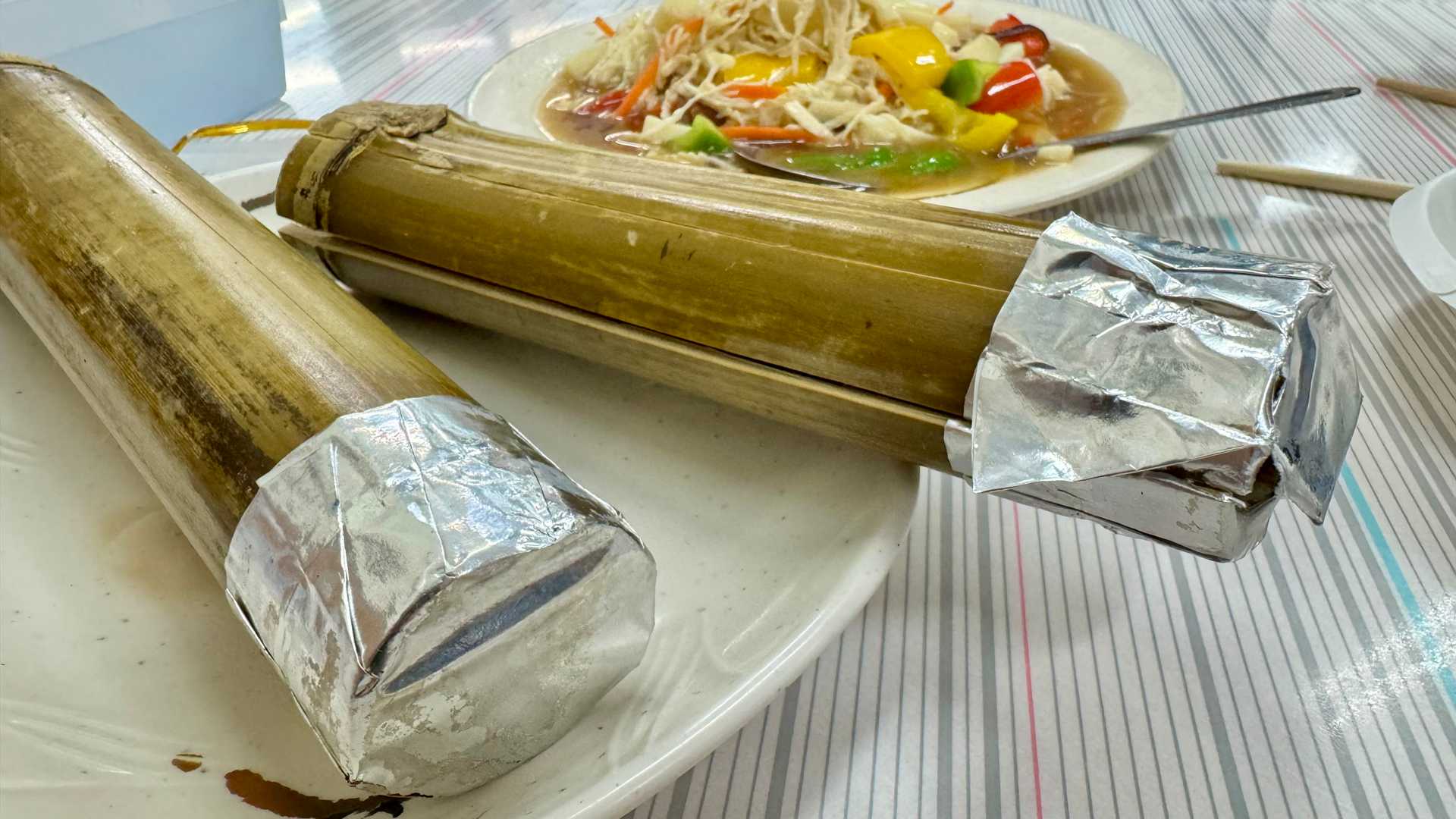 Bamboo rice in the foreground and a salad dish behind it, at an indigenous restaurant at Ita Thao Night Market.