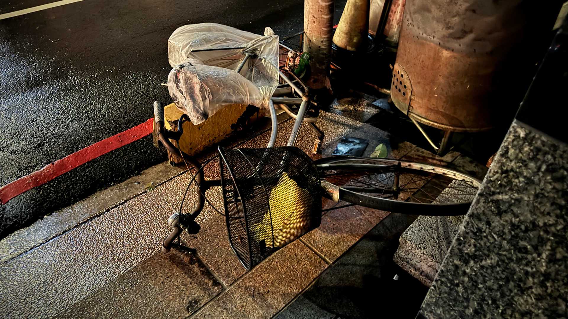 A bicycle on its side on the sidewalk. The seat is wrapped in plastic to protect it from the rain.