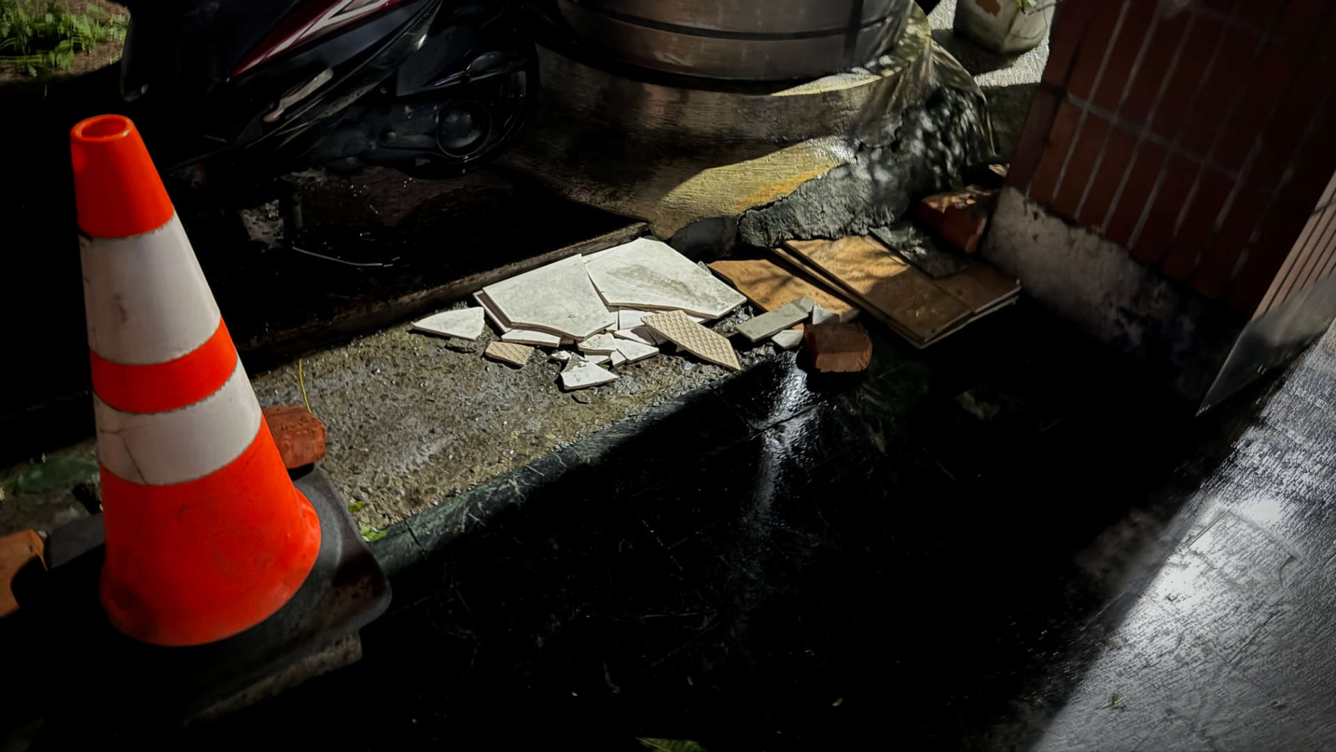 A pile of a few building tiles and some wooden boards next to a road cone.