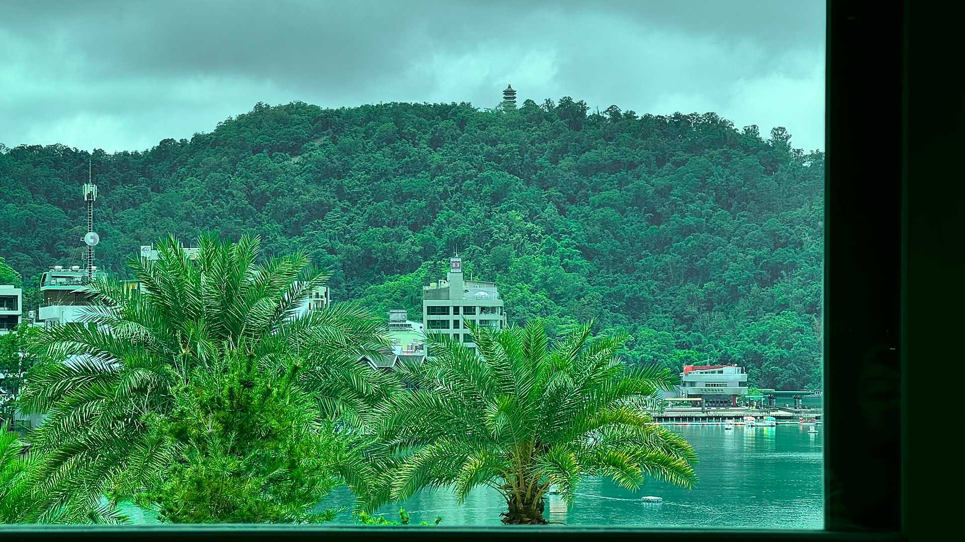 A view through a window, across Sun Moon Lake, to Tzu-En Pagoda – visible on top of a forested hill, perhaps 1km in the distance.