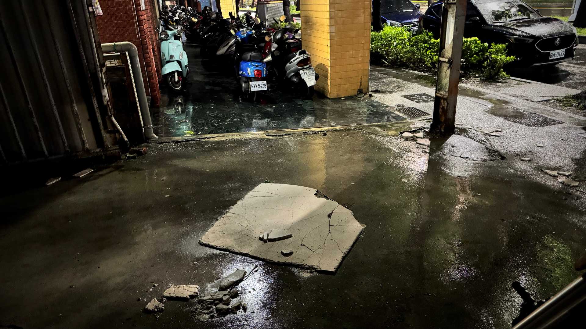 A fallen and partially-smashed wall panel, approximately one meter by one meter, on wet concrete, next to a road in Kaohsiung.