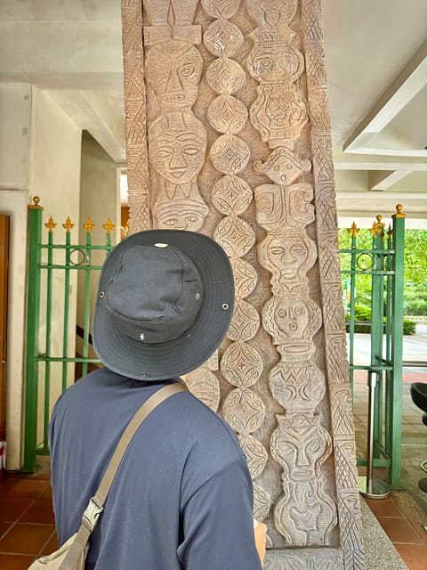 A man inspecting the art carved into a pillar of a building.