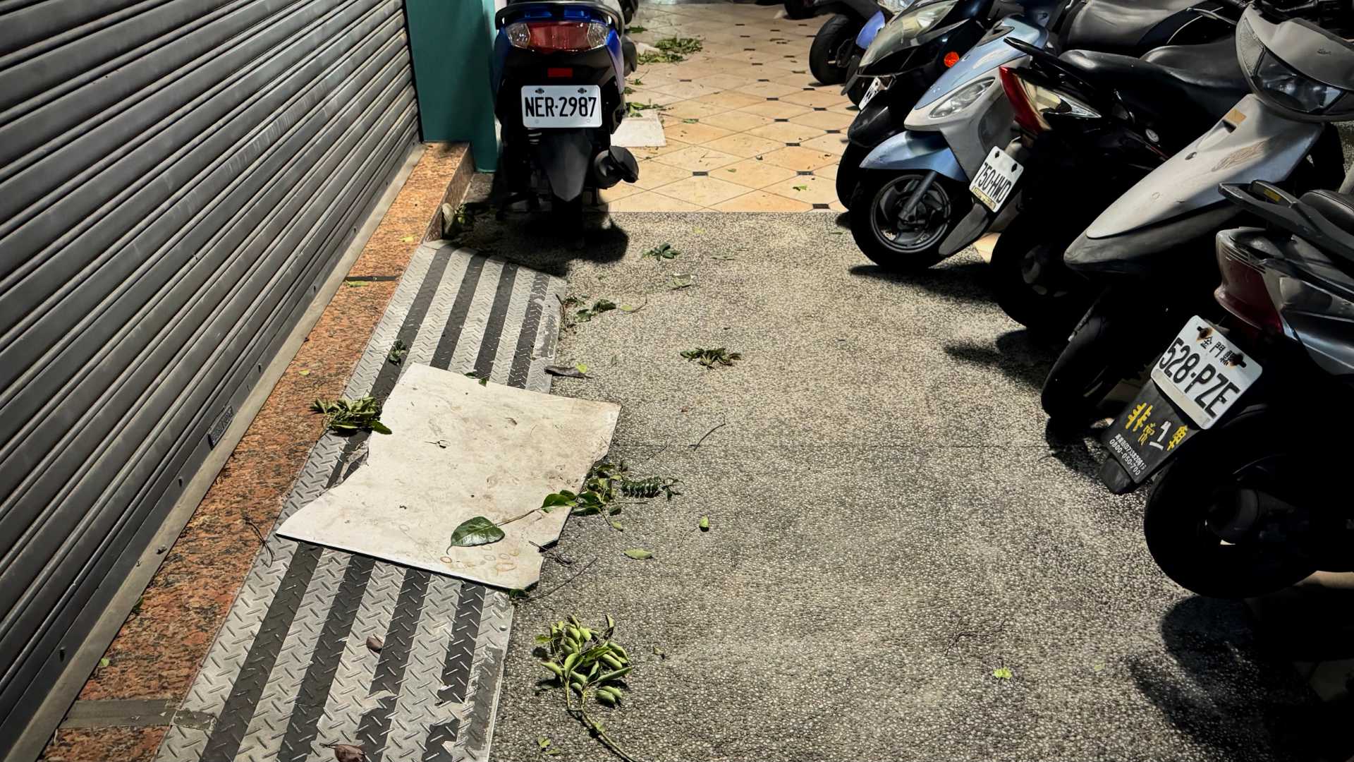 Two fallen panels on the sidewalk in Kaohsiung, Taiwan. The sidewalk is otherwise occupied by a dozen parked scooters.