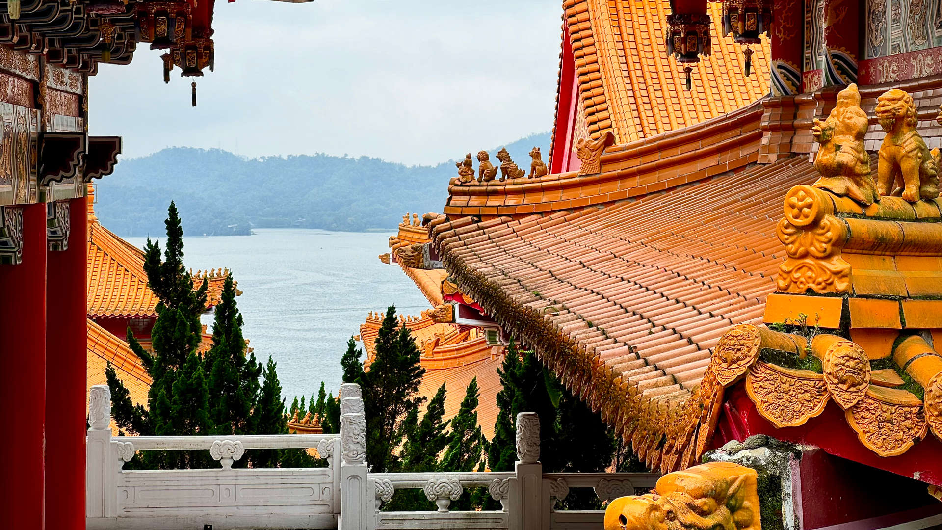 The stepped terracotta tiled roofs of Sun Moon Lake Wenwu Temple, above Sun Moon Lake. The tiles are wet and reflective after recent rain. Small terracotta sculptures of men, lions, and other animals adorn some parts of the rooftops.