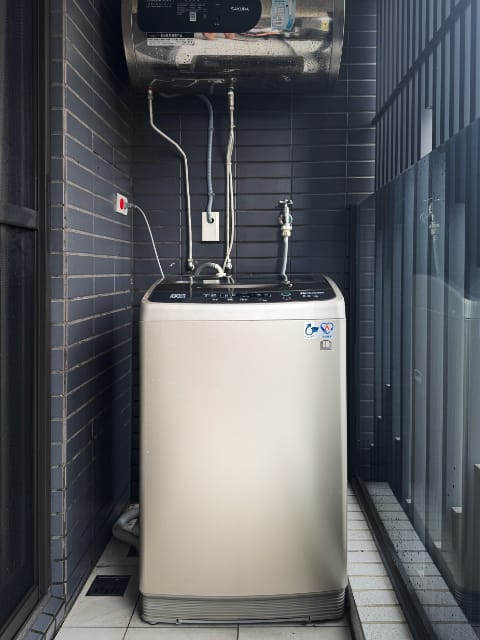 A Sanlux washing machine on a narrow balcony in Taiwan. Above it, a steel cylinder is mounted to the wall.