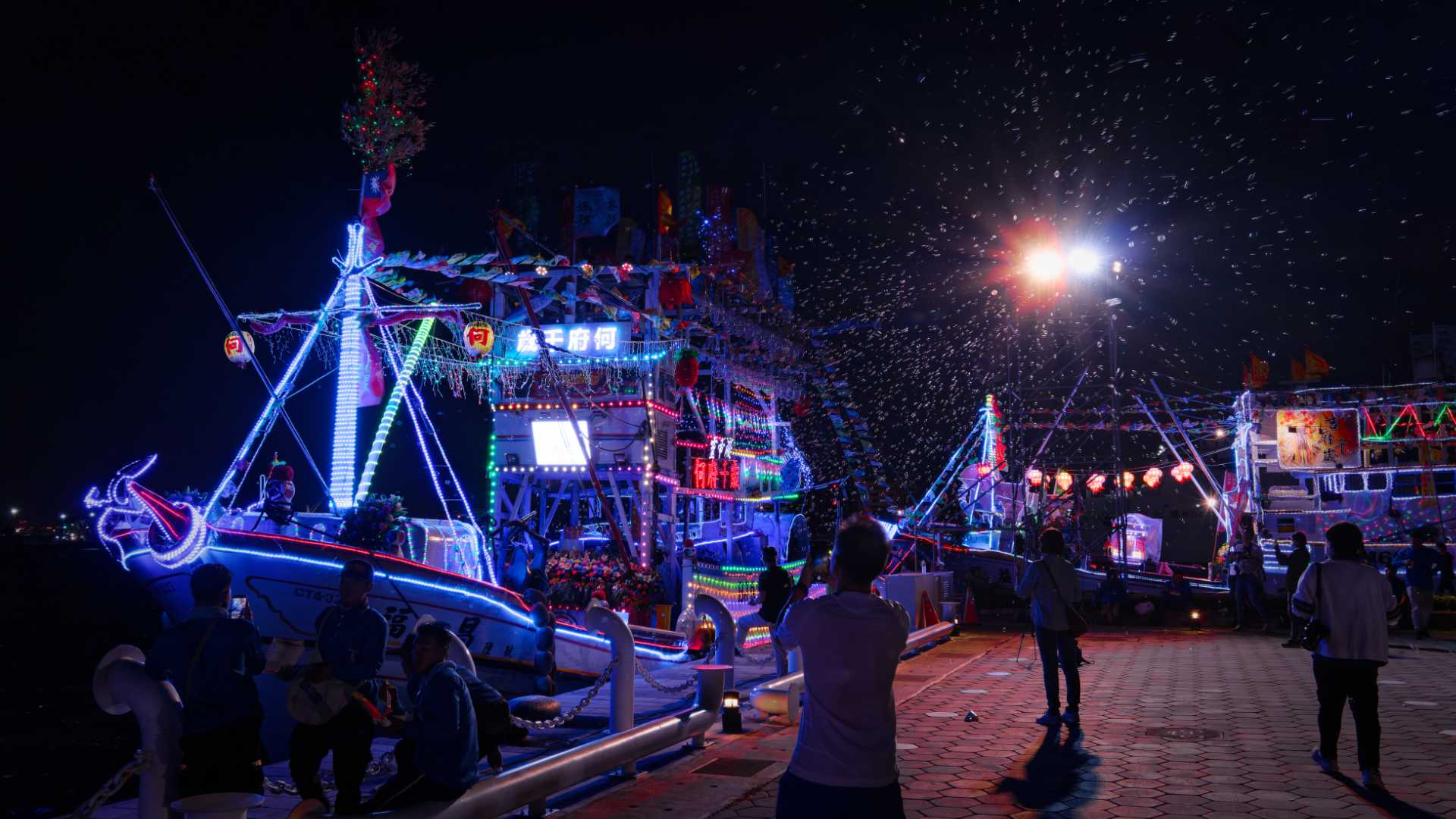 Two boats docked at the corner of Love Pier and Pier-2 in Kaohsiung, Taiwan. One boat has a bubble machine, pumping bubbles into the air. Both boats are brightly decorated.