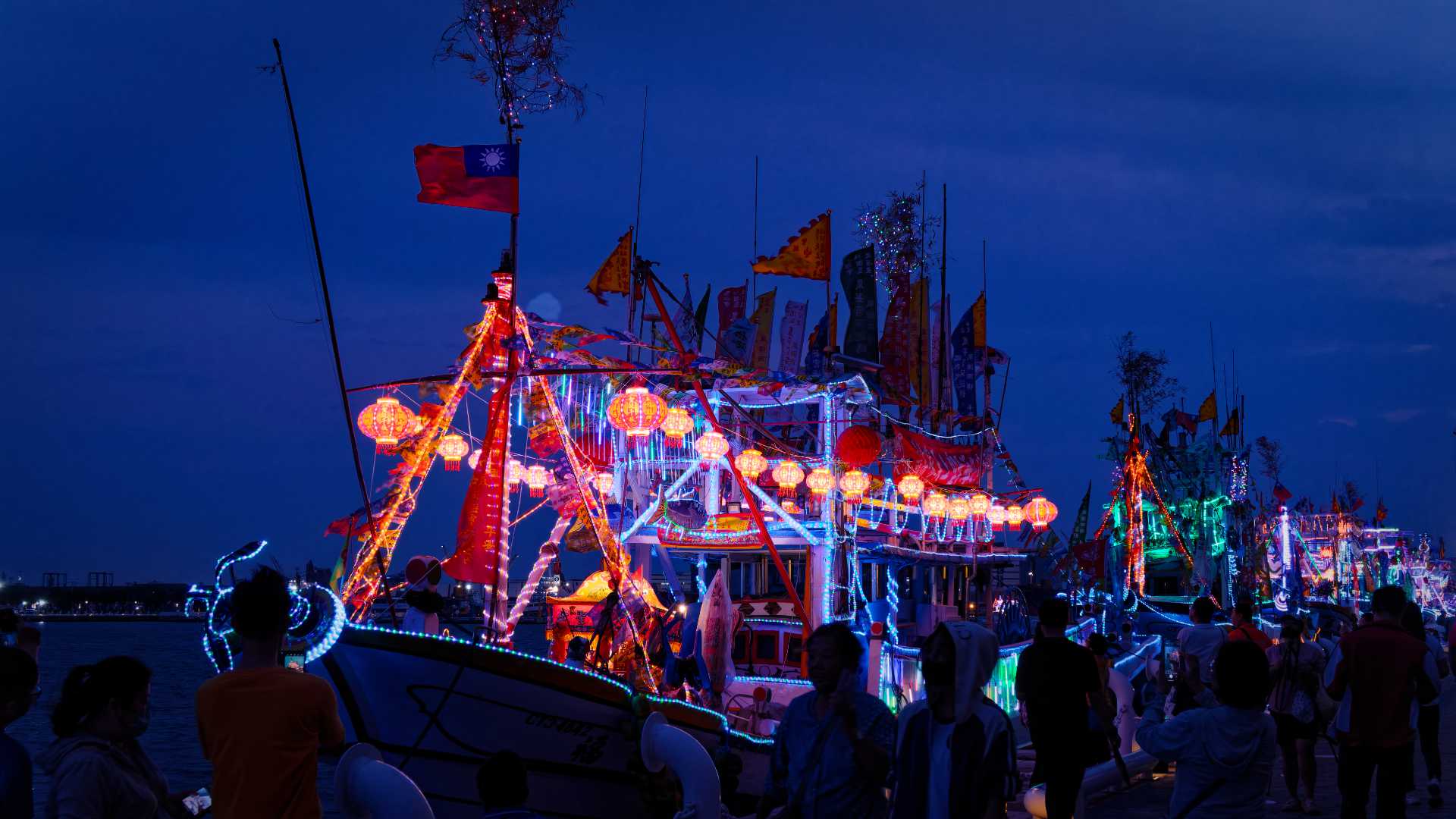 Branches of a tree affixed to the highest point of a mast on a brightly-decorated Taiwanese fishing boat.