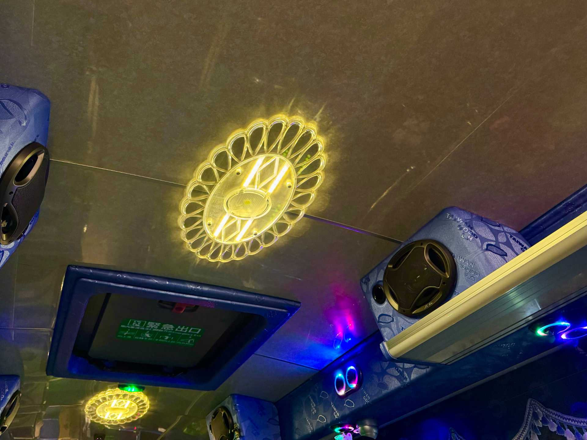 An illuminated clear plastic light fitting on the ceiling of a Taiwanese tour bus. It is in the shape of a doily, but is glowing warm white due to embedded LED lights.