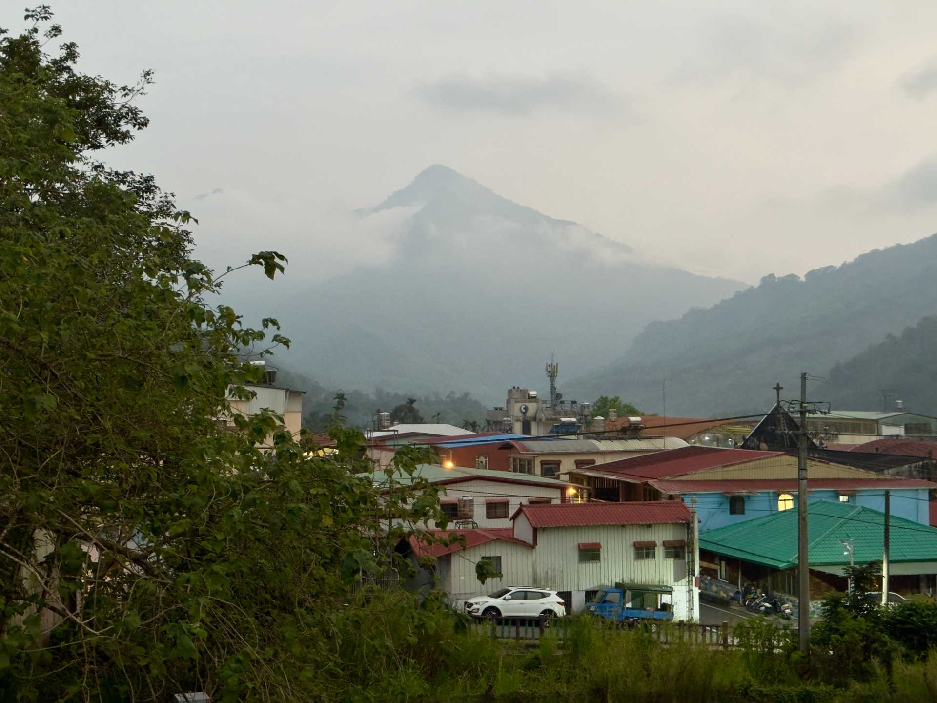 Two forest-clad conical mountains, partially concealed by clouds, in the distance above the iron rooftops of Maya Village.