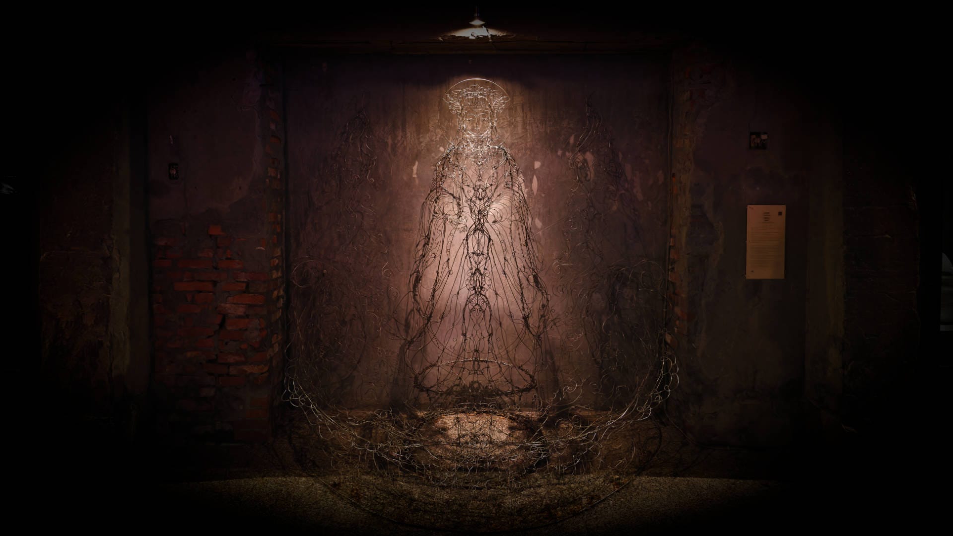 A night-time photo of a wireframe-style sculpture of the sea goddess Mazu, lit from above, in front of an old warehouse wall at the Pier-2 Art Center in Kaohsiung, Taiwan.