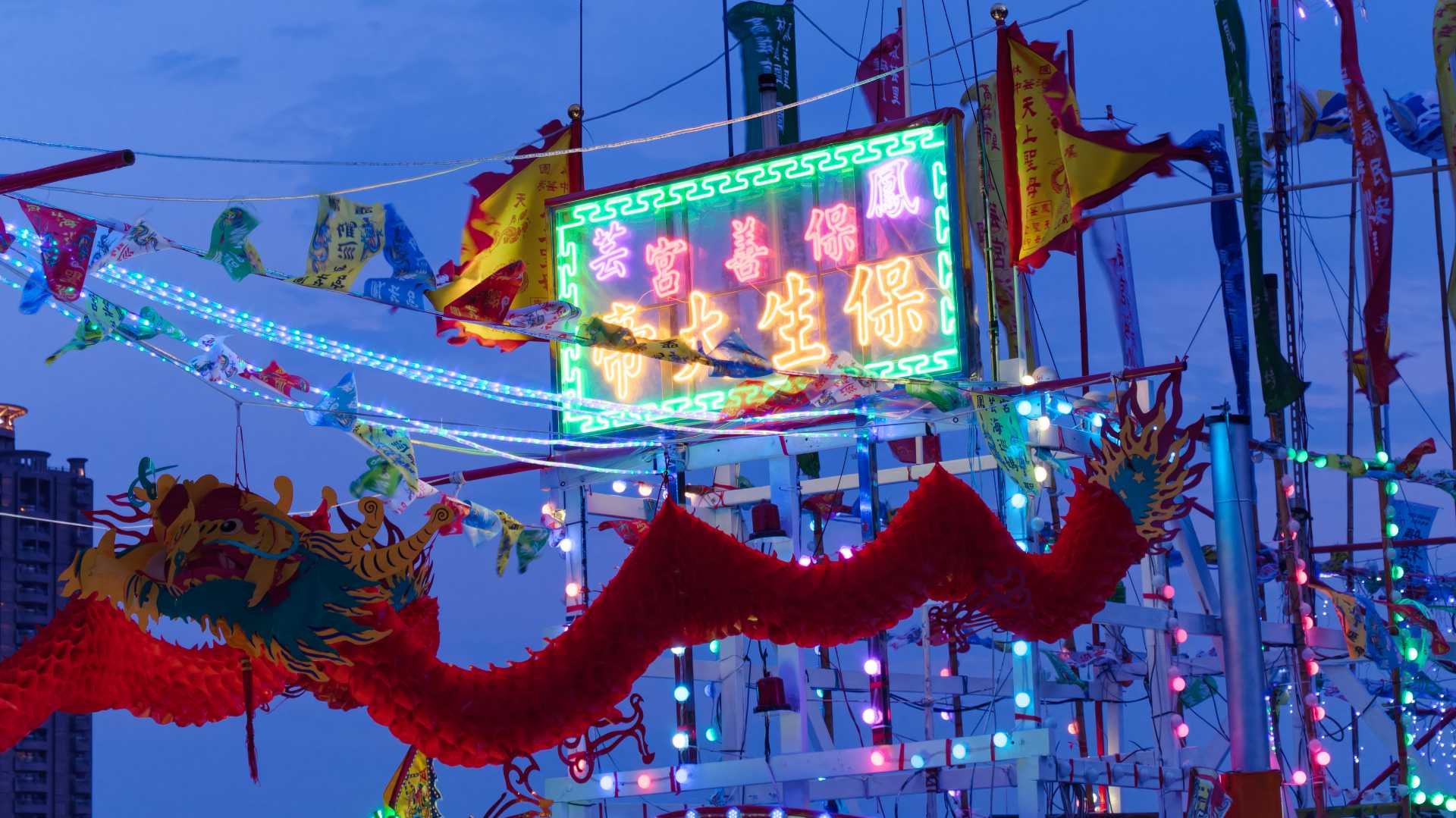 A neon sign installed on a Taiwanese fishing boat. Behind it are two yellow flags, and below it two hanging dragons.
