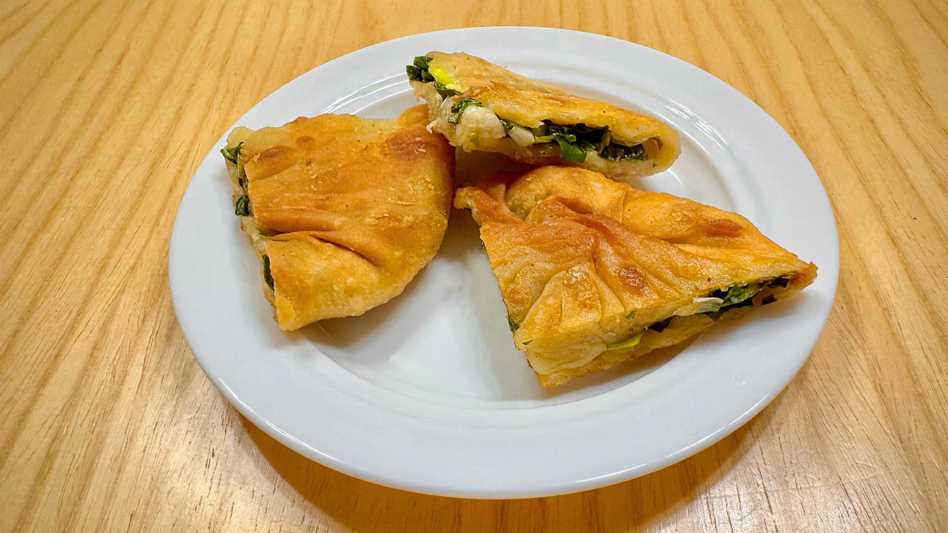 Three pieces of a Taiwanese green onion pancake, sliced into quarters, on a clean white plate on a wooden table.