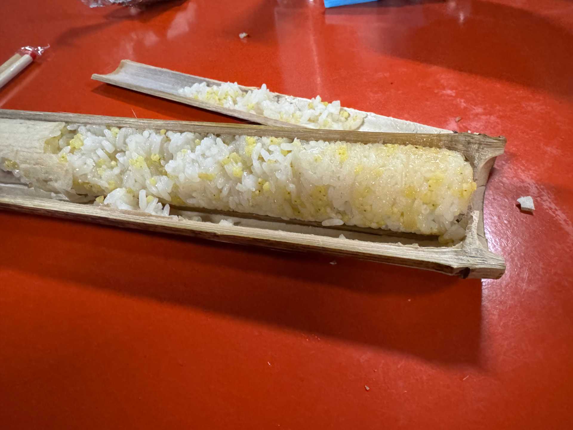 A cracked-open piece of roasted bamboo, with densely-stuffed rice inside. The rice is mixed with yellowish millet.