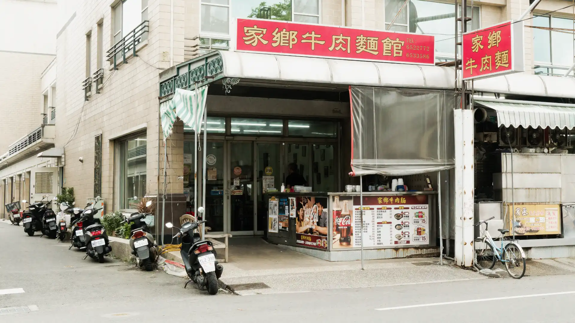 Exterior of Jiaxiang Beef Noodle Restaurant on a quiet street corner in Tainan City. A bicycle and half a dozen motorbikes are parked outside.