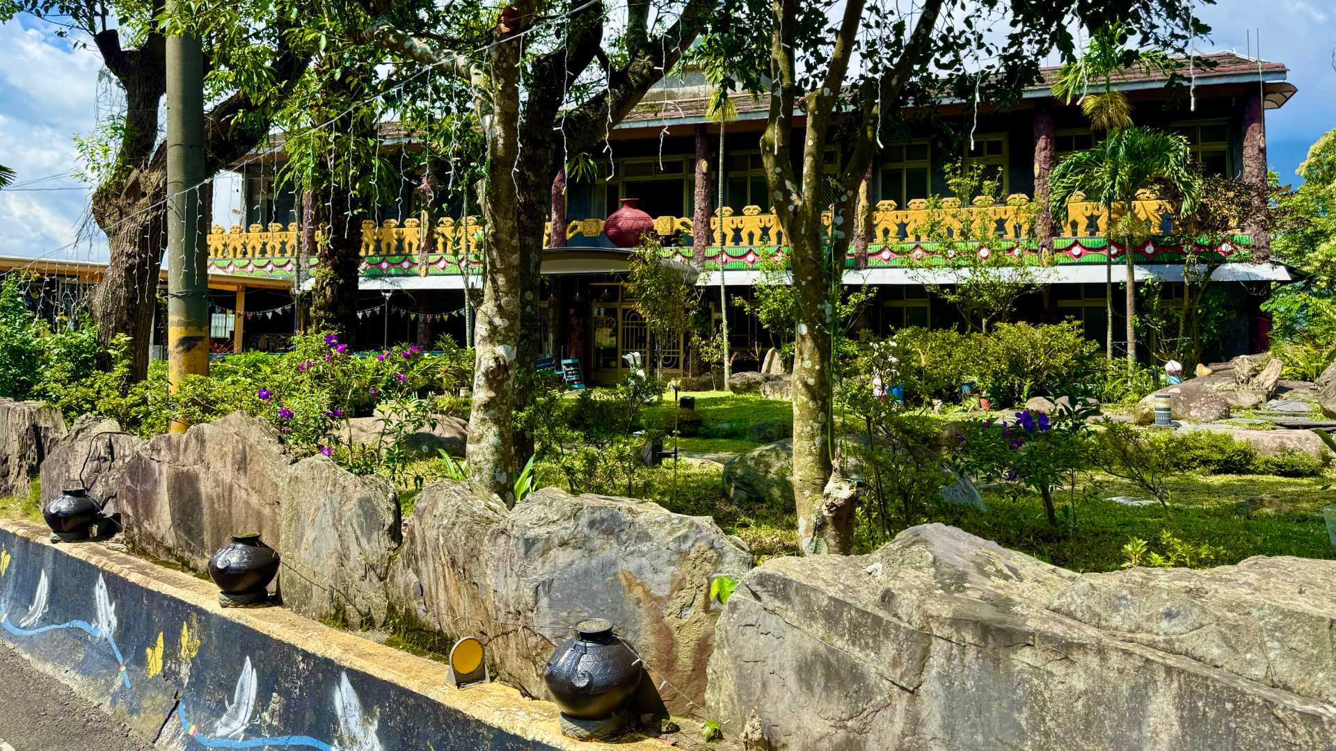 Salrabu Homestay in Wutai, Taiwan. It is heavily decorated with local indigenous Rukai motifs and clay pots, and has a large shaded garden in front. It looks like a welcoming, restful place.