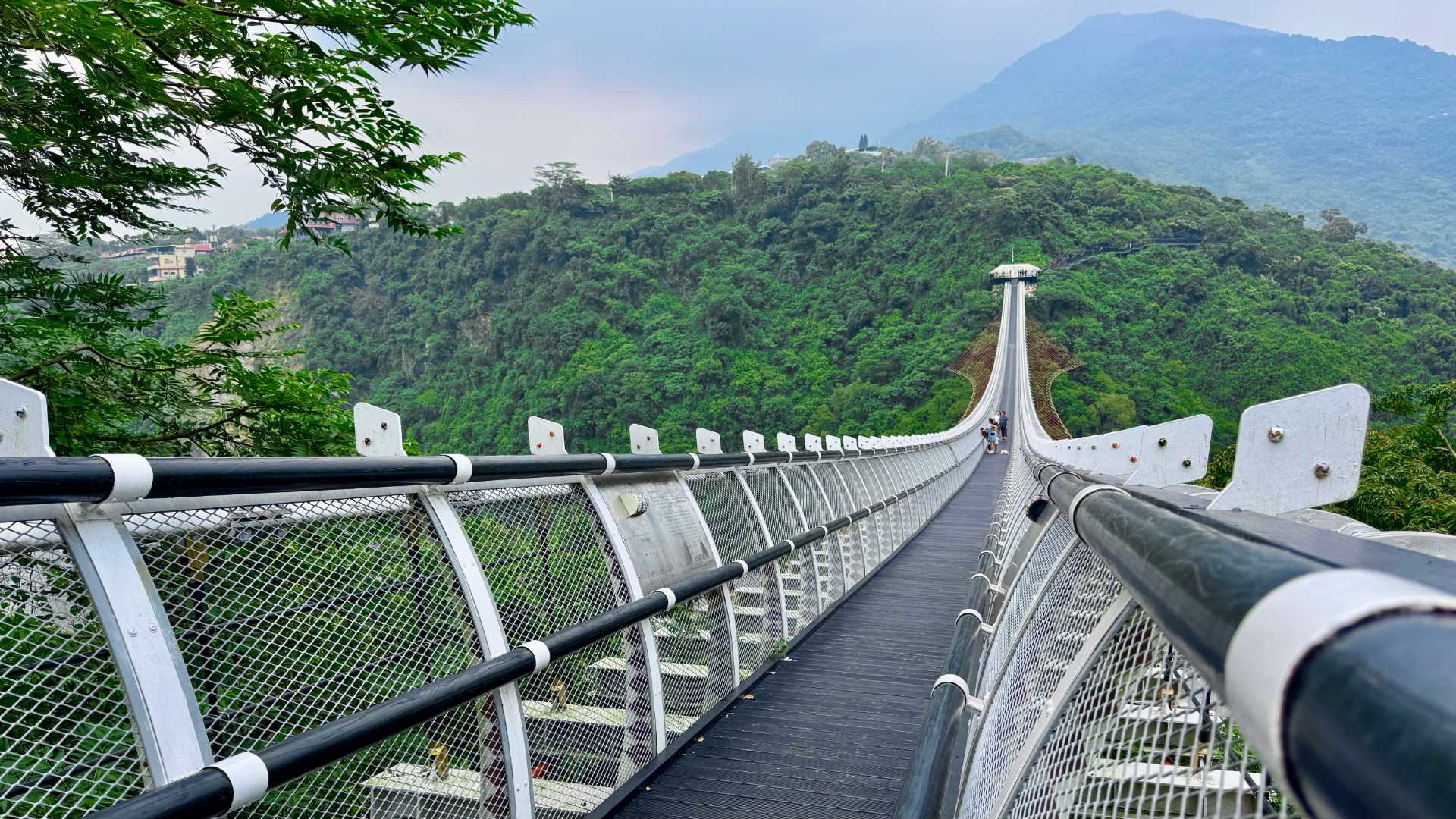 A long hammock-style suspension bridge stretching into the distance across a steep mountain valley in Pingtung County, Taiwan.