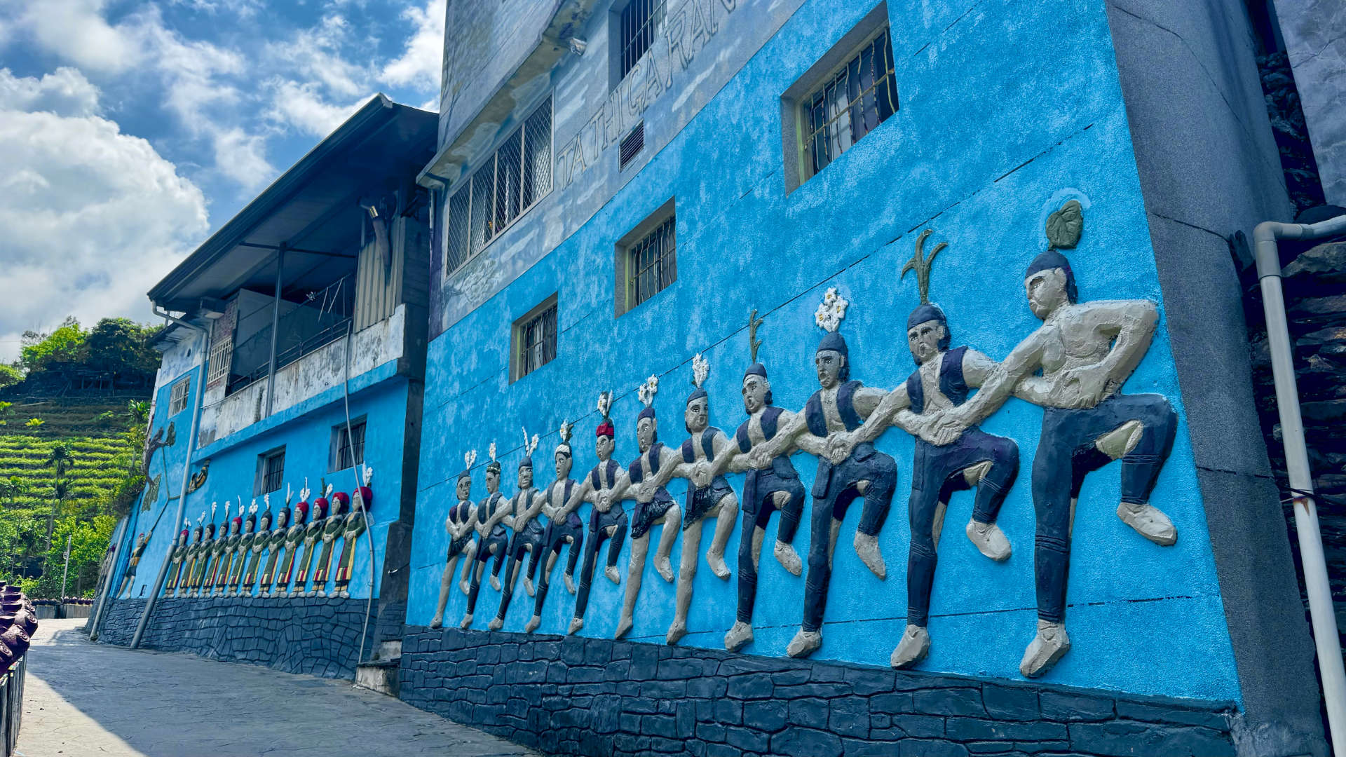 A sculpted relief along the ground floor of a large building in Wutai Township, Taiwan. It delicts men and women dancing in indigenous Rukai attire.