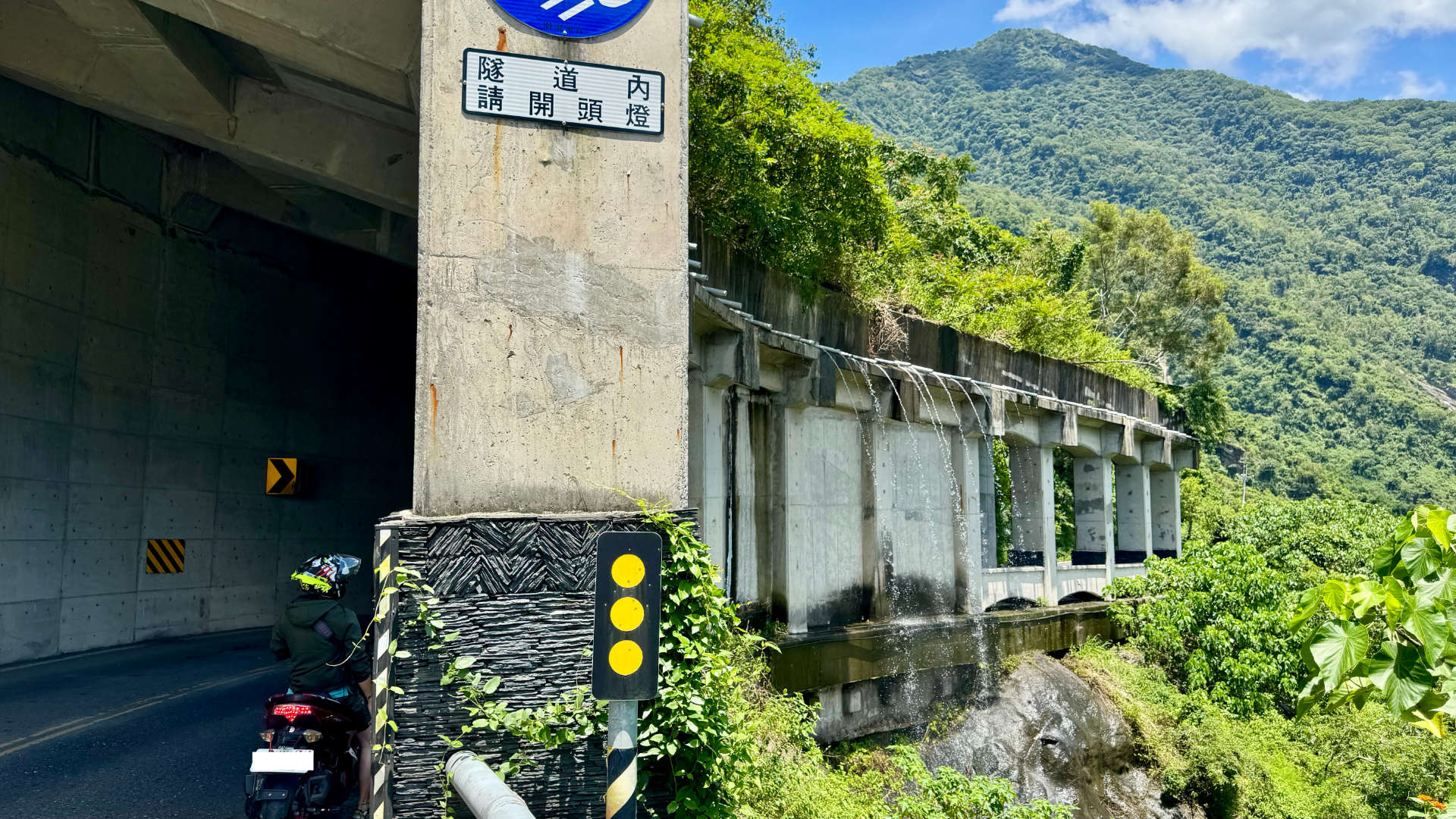 A road tunnel along the edge of a mountain in Pingtung County, Taiwan. Water is cascading down one side of the tunnel.