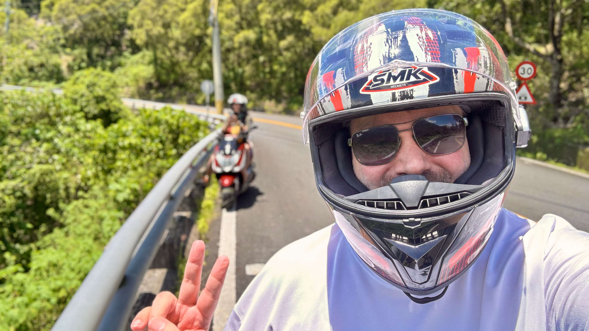 A selfie of the author wearing a motorcycle helmet and giving a peace sign, with another rider in the distance, stopped at the side of a mountain road in Pingtung County, Taiwan.