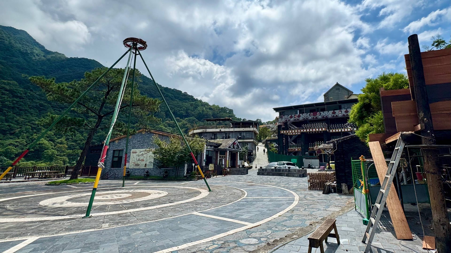 A pyramid-shaped ceremonial structure in the middle of a public square, with ornately-decorated buildings and mountains beyond.