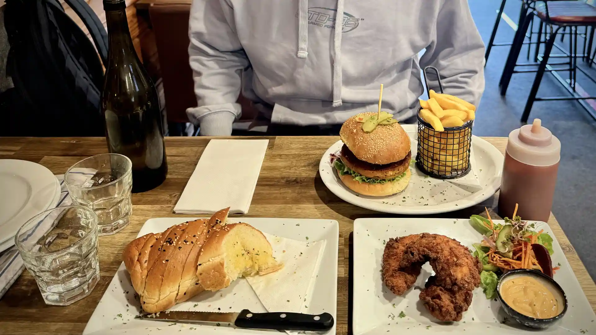 Three dishes on a table in a pub, comprising one garlic bread, one burger with fries, and some fried chicken with salad.