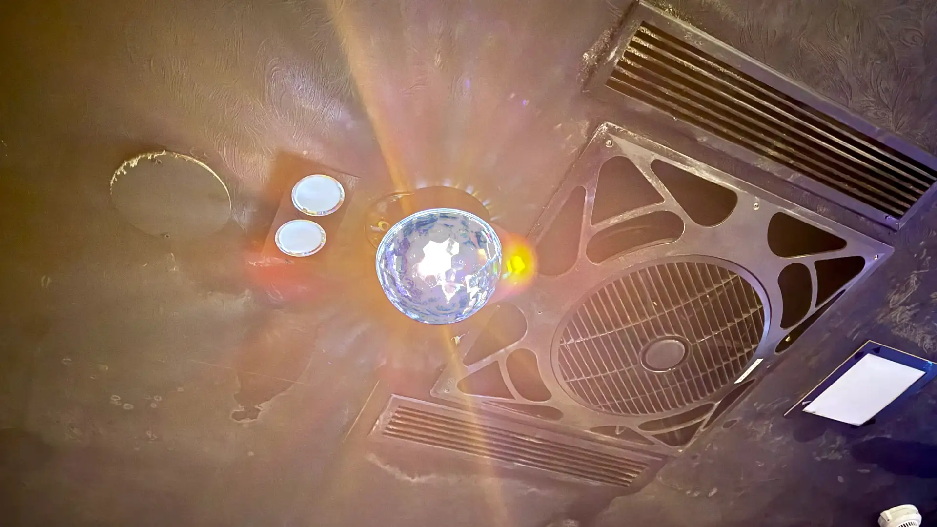 A disco ball mounted to a ceiling, next to a powerful airconditioner.