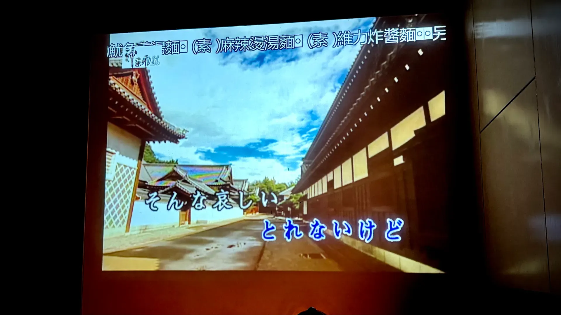 A Japanese music video being projected onto a wall, with karaoke-style lyrics superimposed.