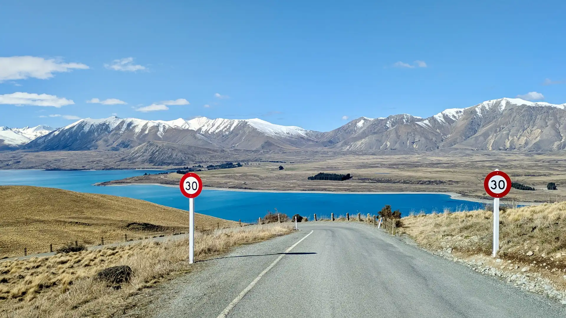 A view of Lake Tekapo with snowy mountains beyond, taken looking downhill from the road to the Mount John Observatory.