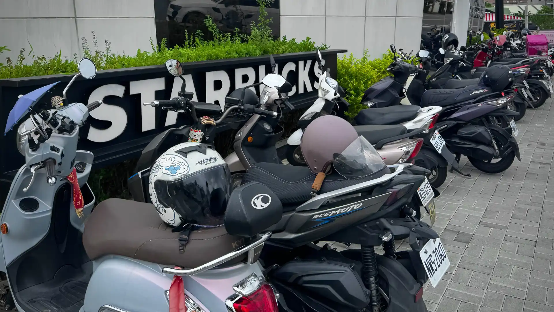 A row of a dozen or so scooters parked on the pavement outside a Starbucks cafe in Taiwan.
