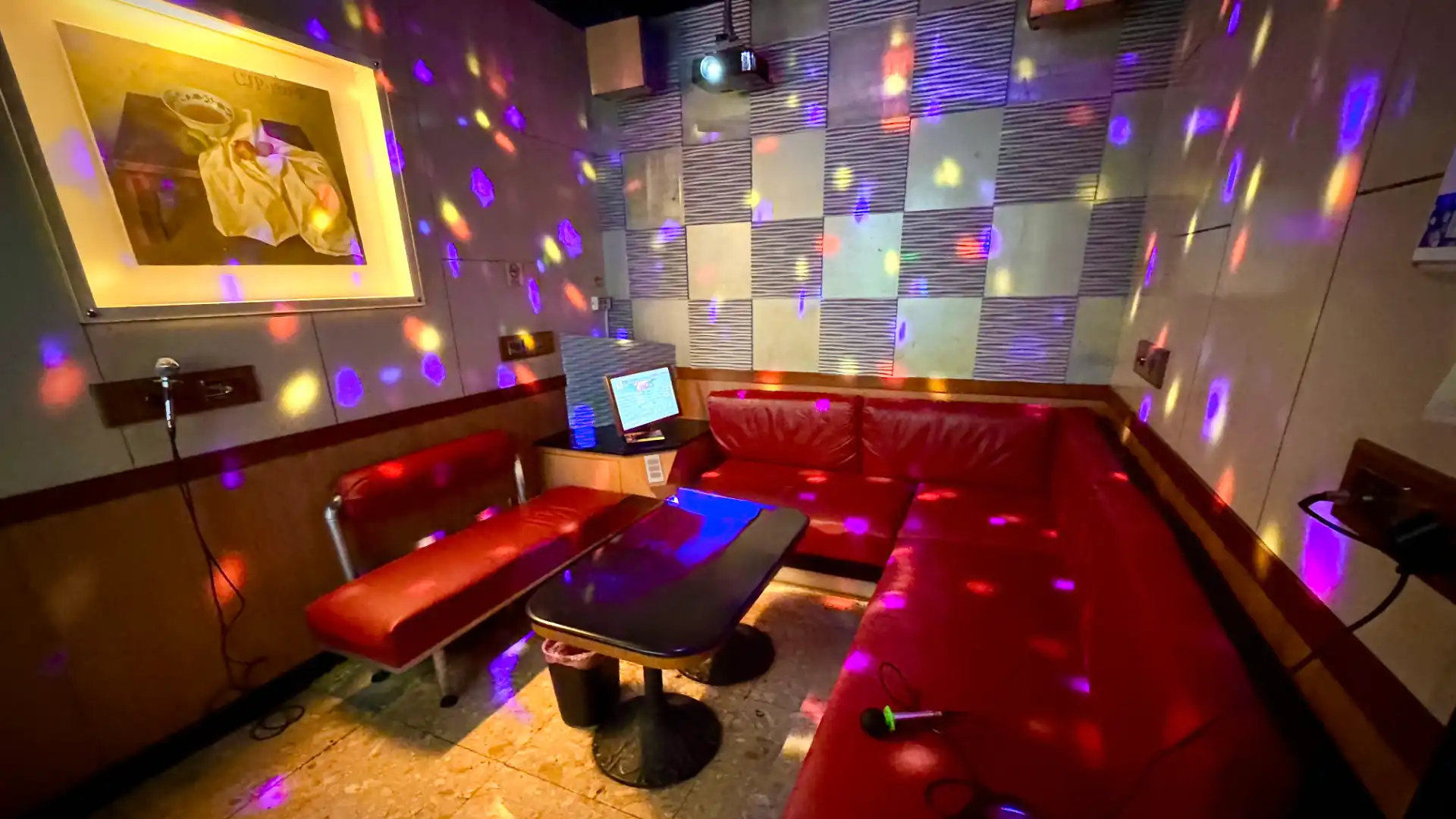 Interior of a private KTV room in Taiwan. A large red sofa wraps around three sides of the room, which is lit by disco ball lighting.