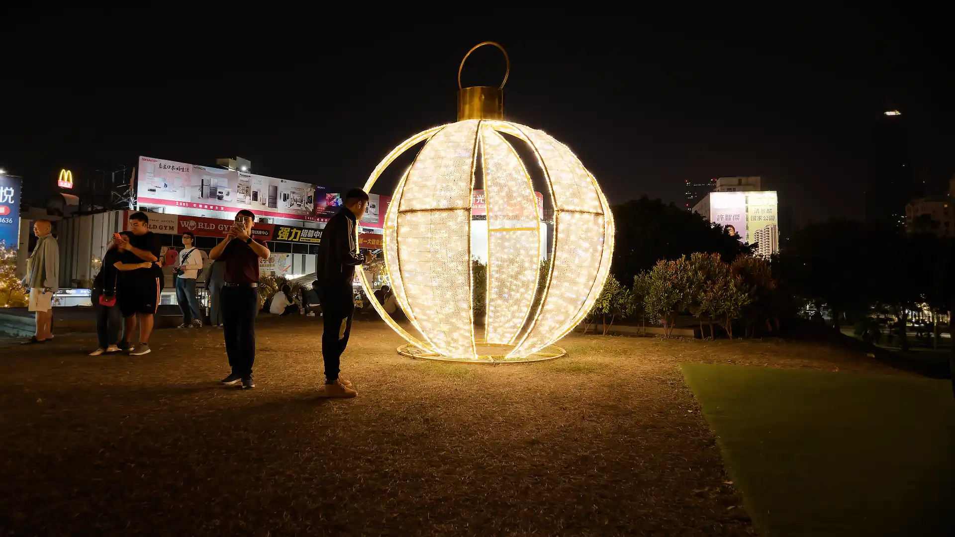 A giant illuminated Christmas ornament, maybe three meters tall, resting on a grass mound.