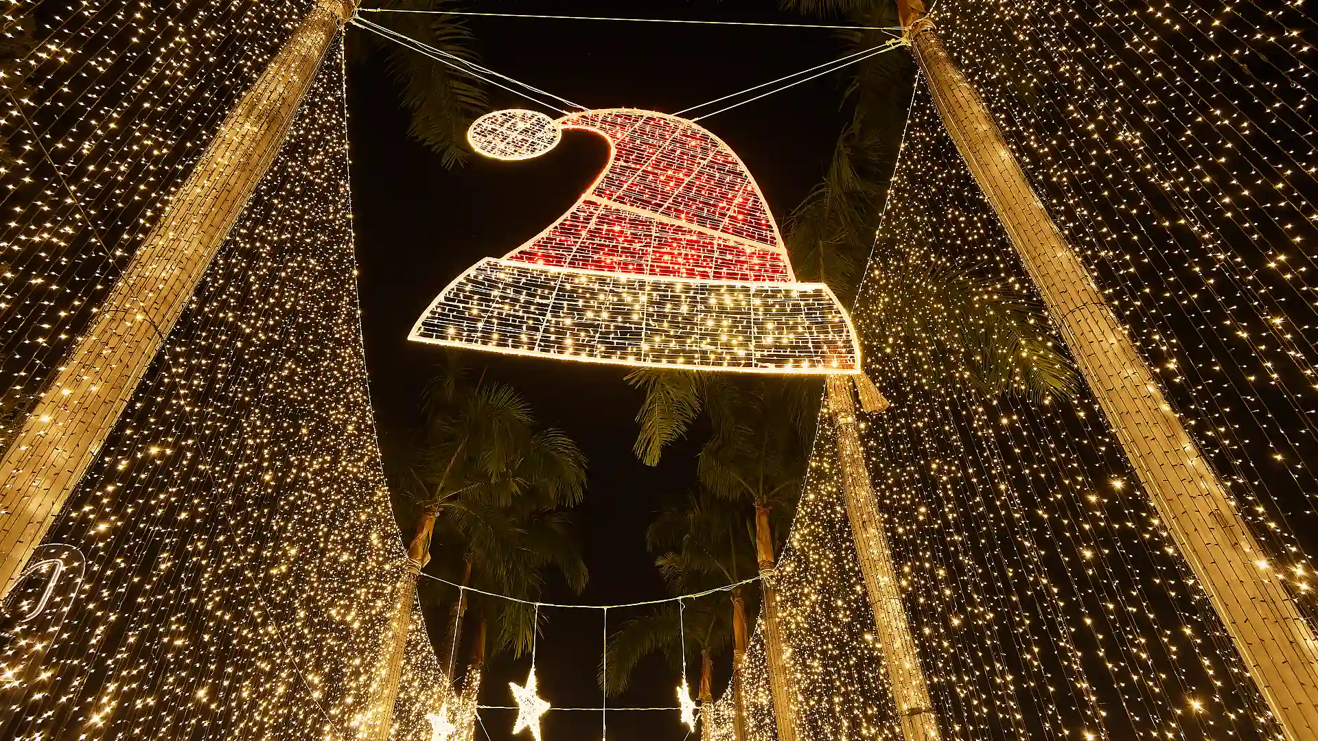 A red and white Santa hat made of hundreds of small lights hanging in the sky.