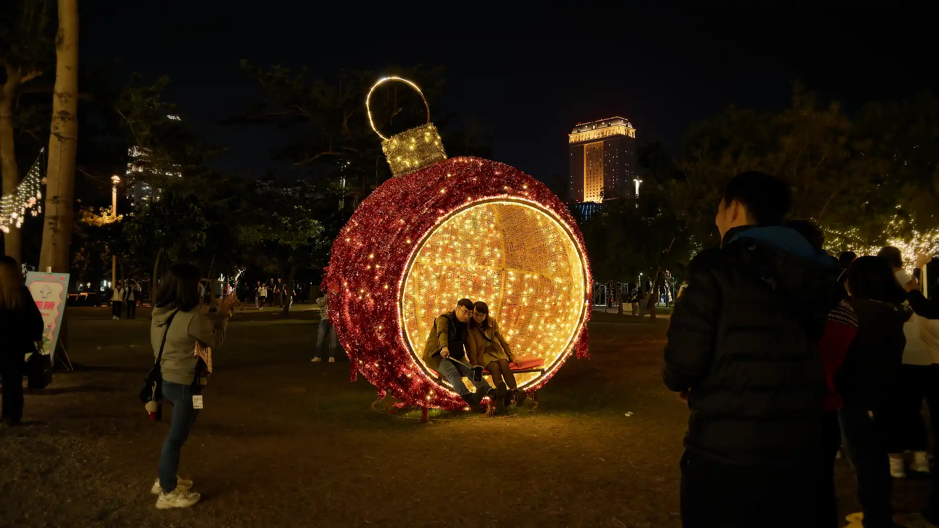 A couple taking a selfie inside a giant illuminated Christmas ornament.