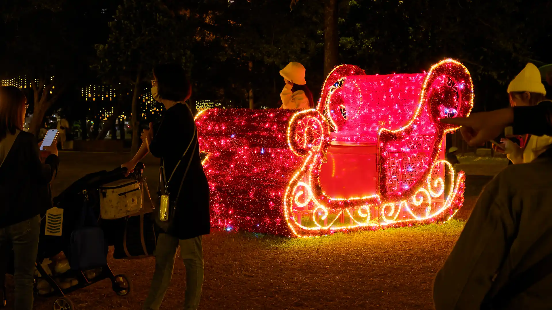 A woman poses for a photo while sitting in an illuminated red and white sleigh.