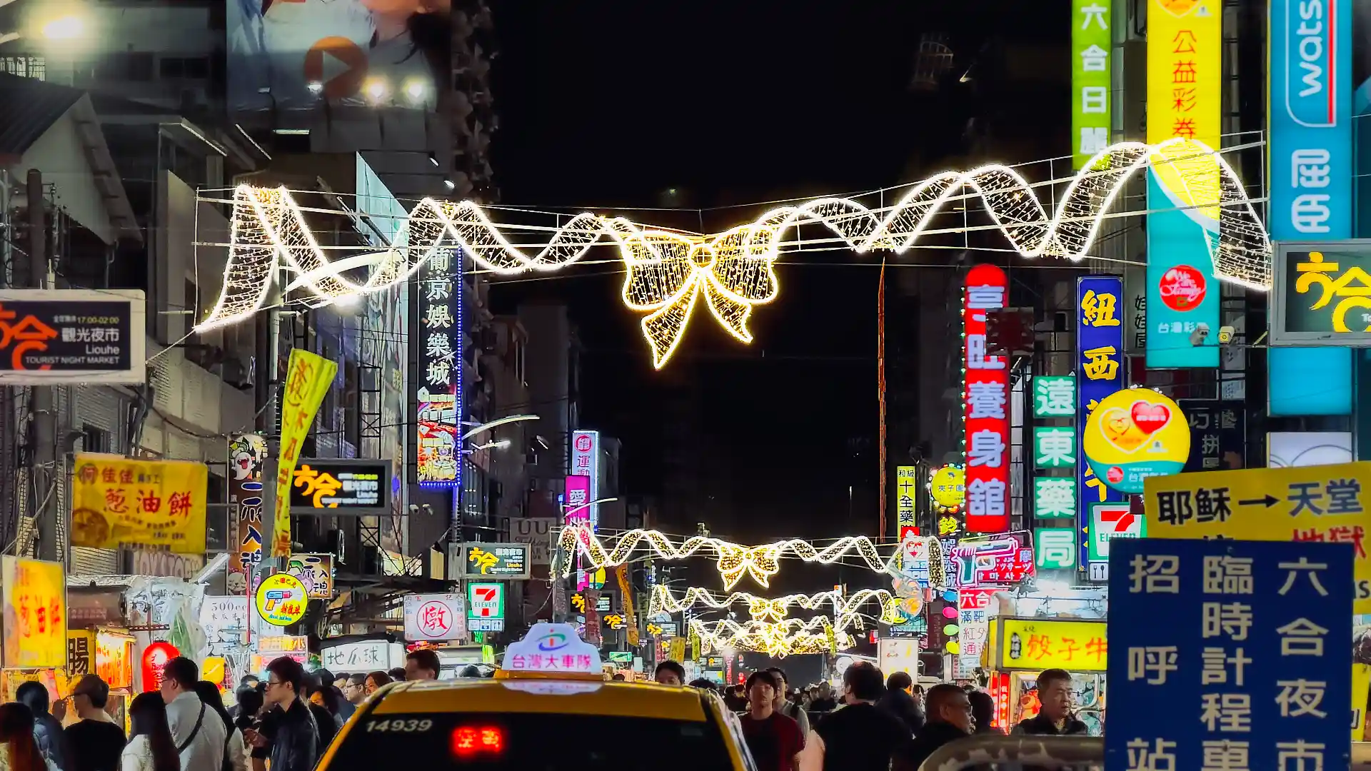 Christmas lights hanging above Liouhe (Liuhe) Night Market. The market is crowded with people and food stalls.