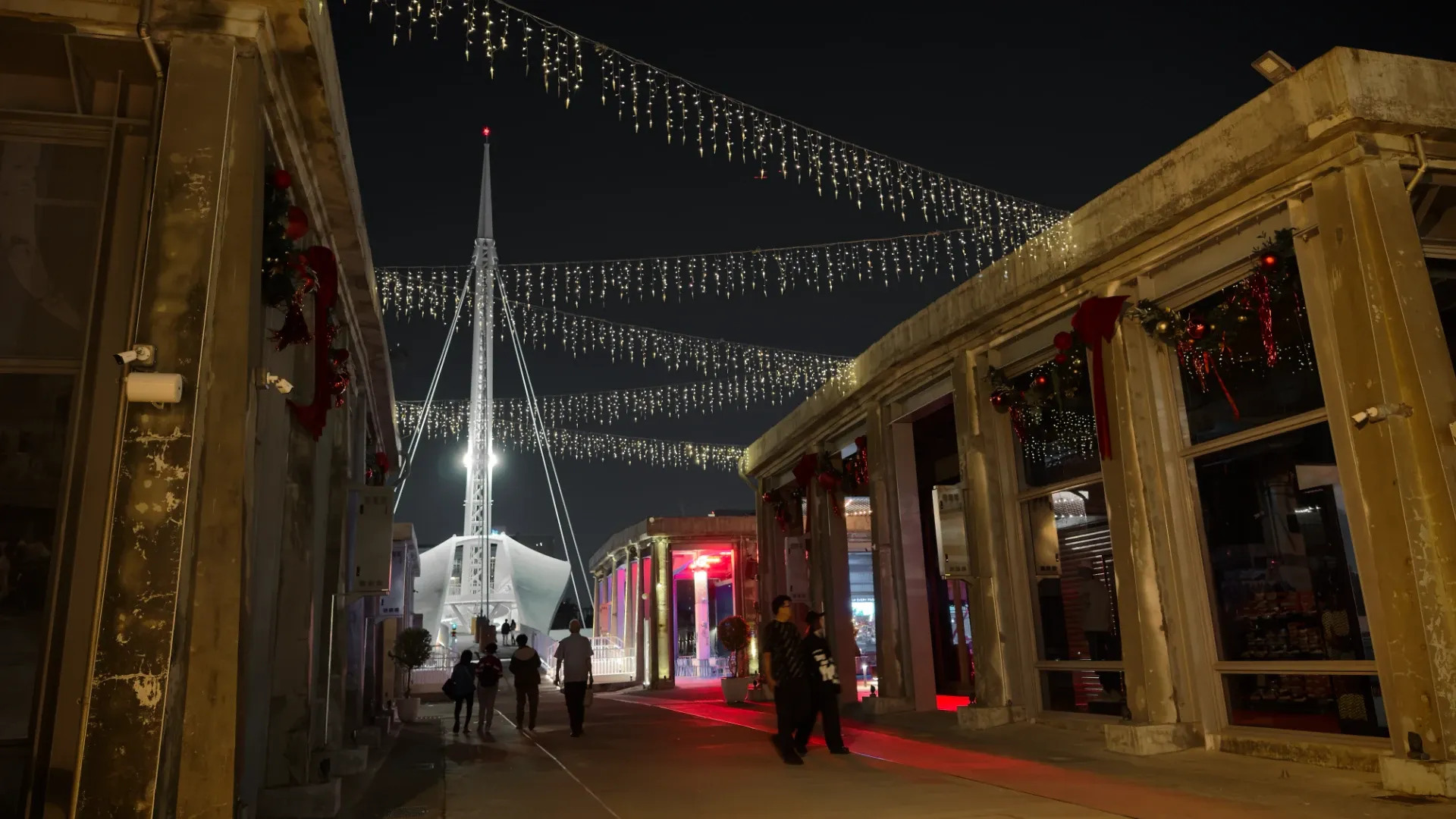 Great Harbor Bridge at Pier 2, Kaohsiung, is illuminated in white in the background behind string lights and Christmas decorations on the foreground buildings.