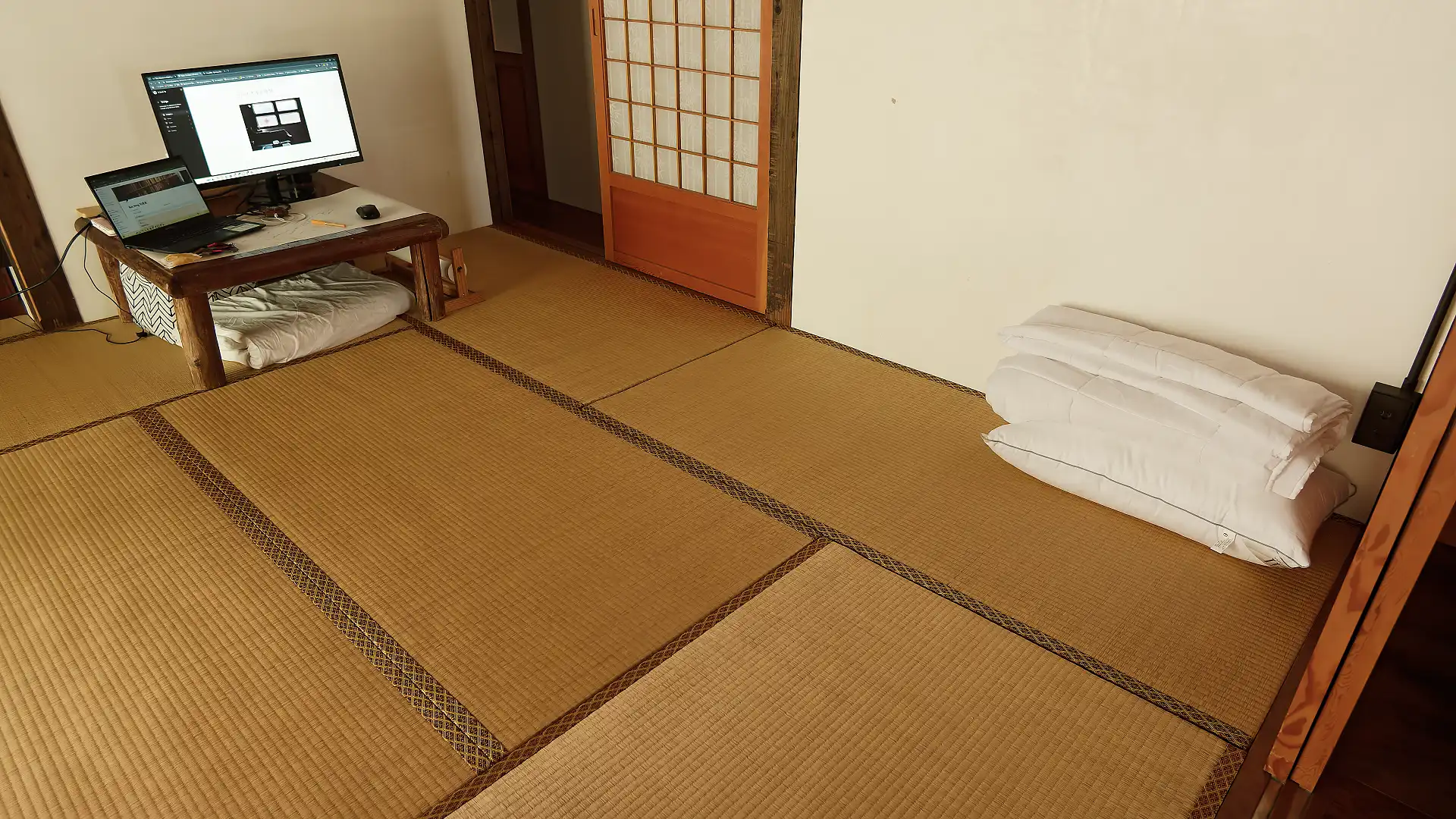 Wide-angle view of a tatami room with a computer on a low table at the far end.