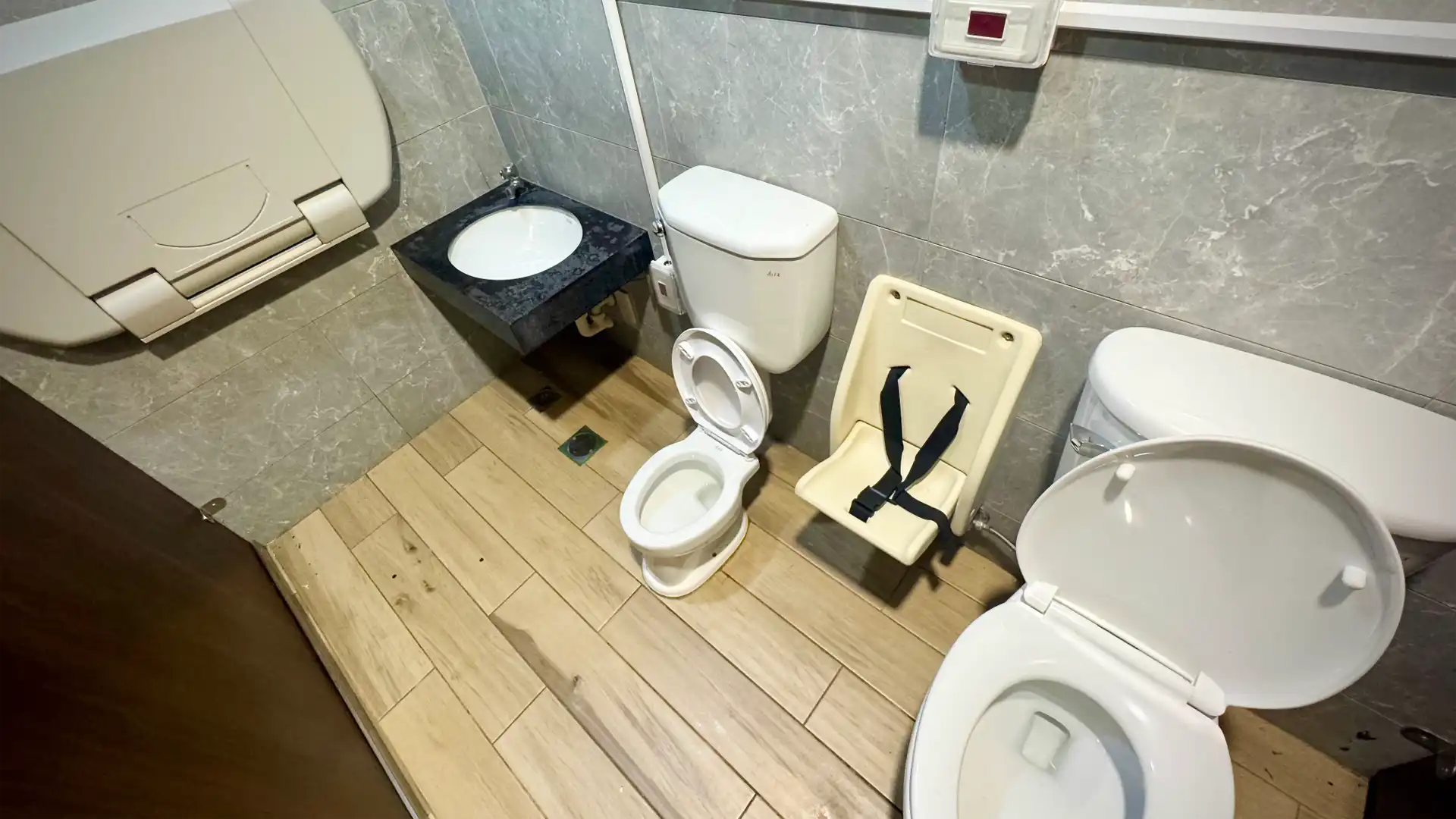 A very clean public bathroom stall containing one regular sitting toilet alongside a half-size (fully-functional) child toilet and a low handbasin for children to watch their hands.