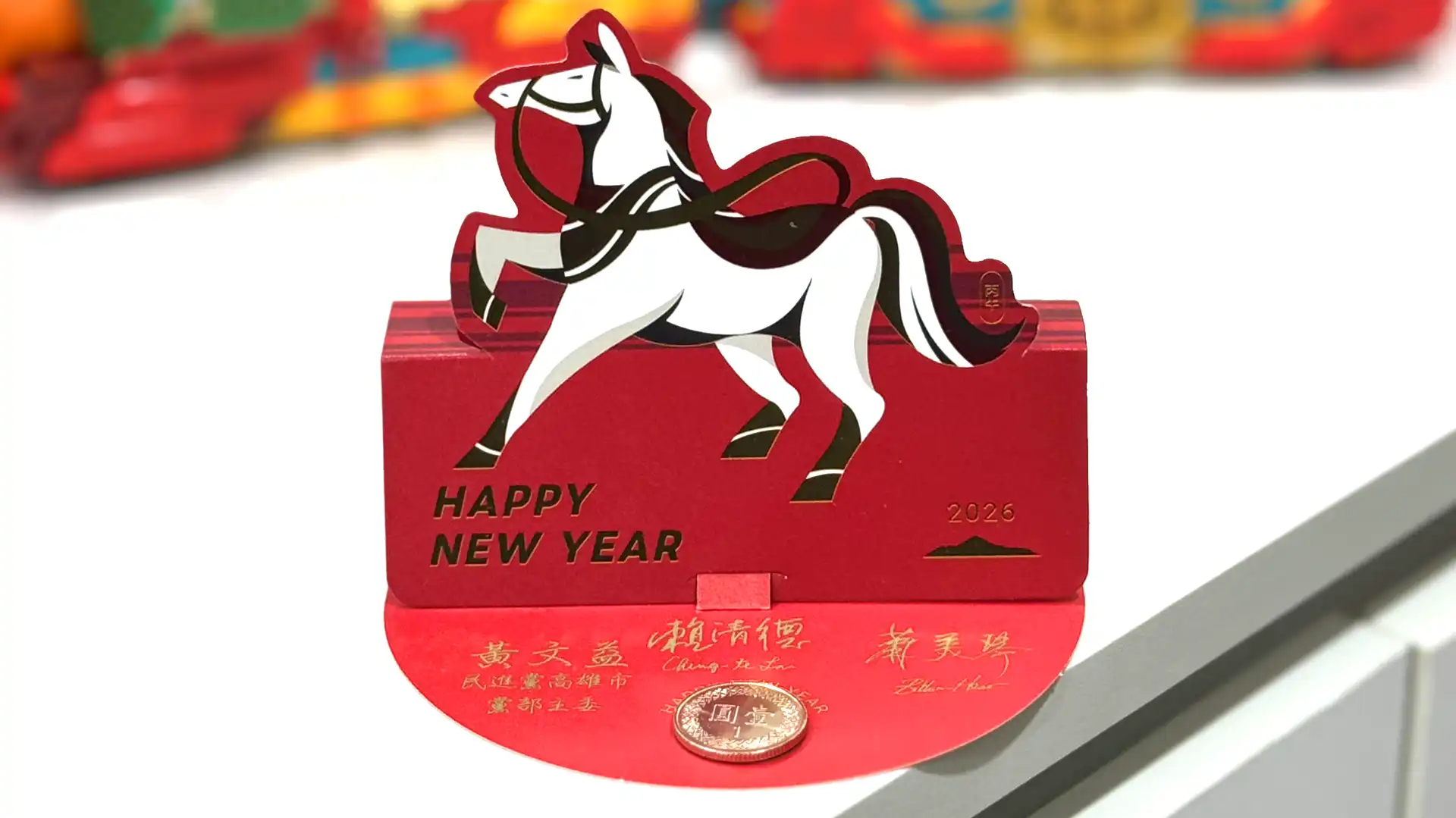 A so-called red envelope, which looks like a pop-up horse on a cardboard platform that has a freshly-minted one New Taiwan Dollar coin stuck onto it, along with three printed signatures.