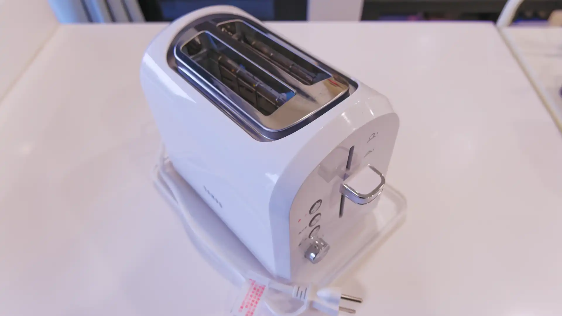 A simple white toaster sitting unplugged on a kitchen bench.