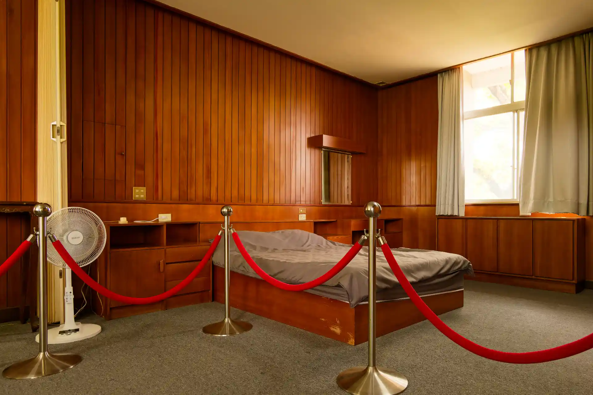 A double bed on wooden bed base, with inbuilt bedside cabinets either side. The bed is behind a velvet rope.