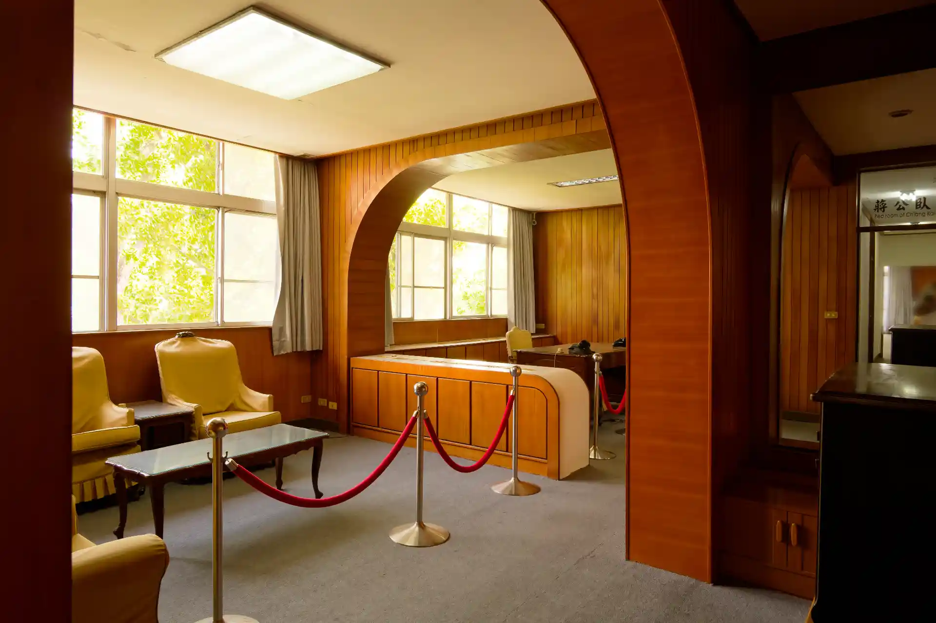 A wide-angle view of Chiang Kai-Shek’s bedroom suite. To the left are two sets of lounge chairs and three coffee tables. Beyond them is an office area with inbuilt storage cabinets and an old wooden desk.